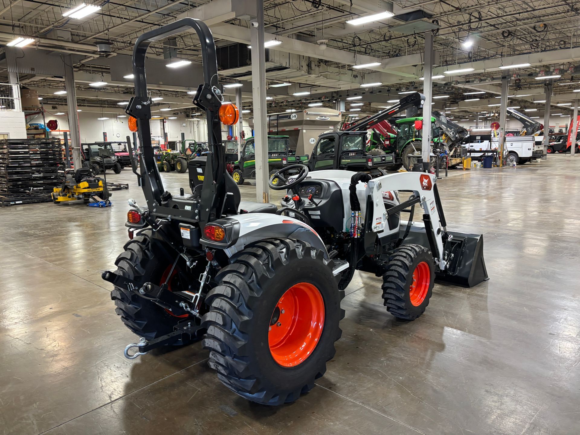 White Bobcat tractor with orange wheels and black roll bar, inside a large building.