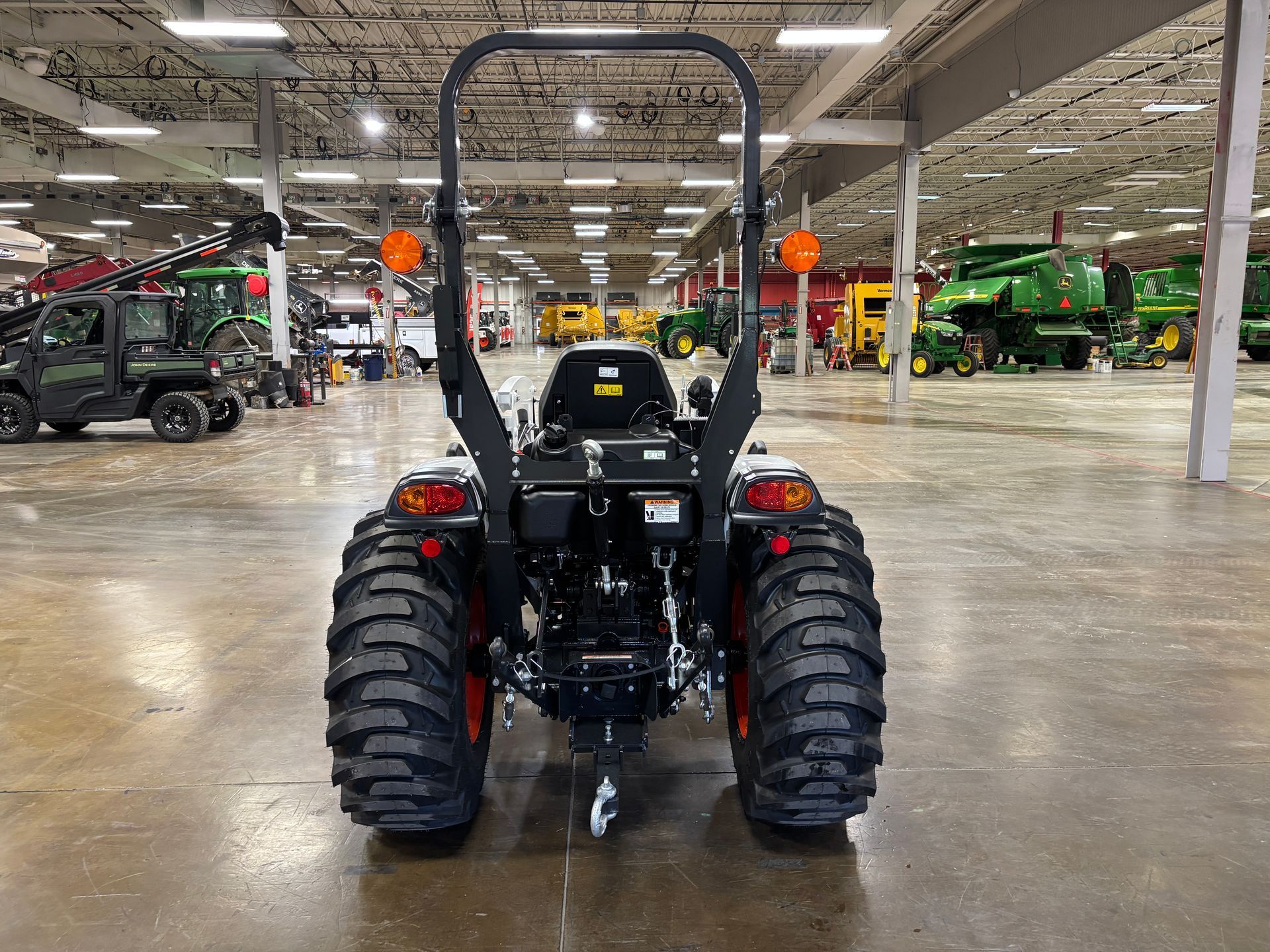 Rear view of a black tractor with large tread tires inside a large warehouse.