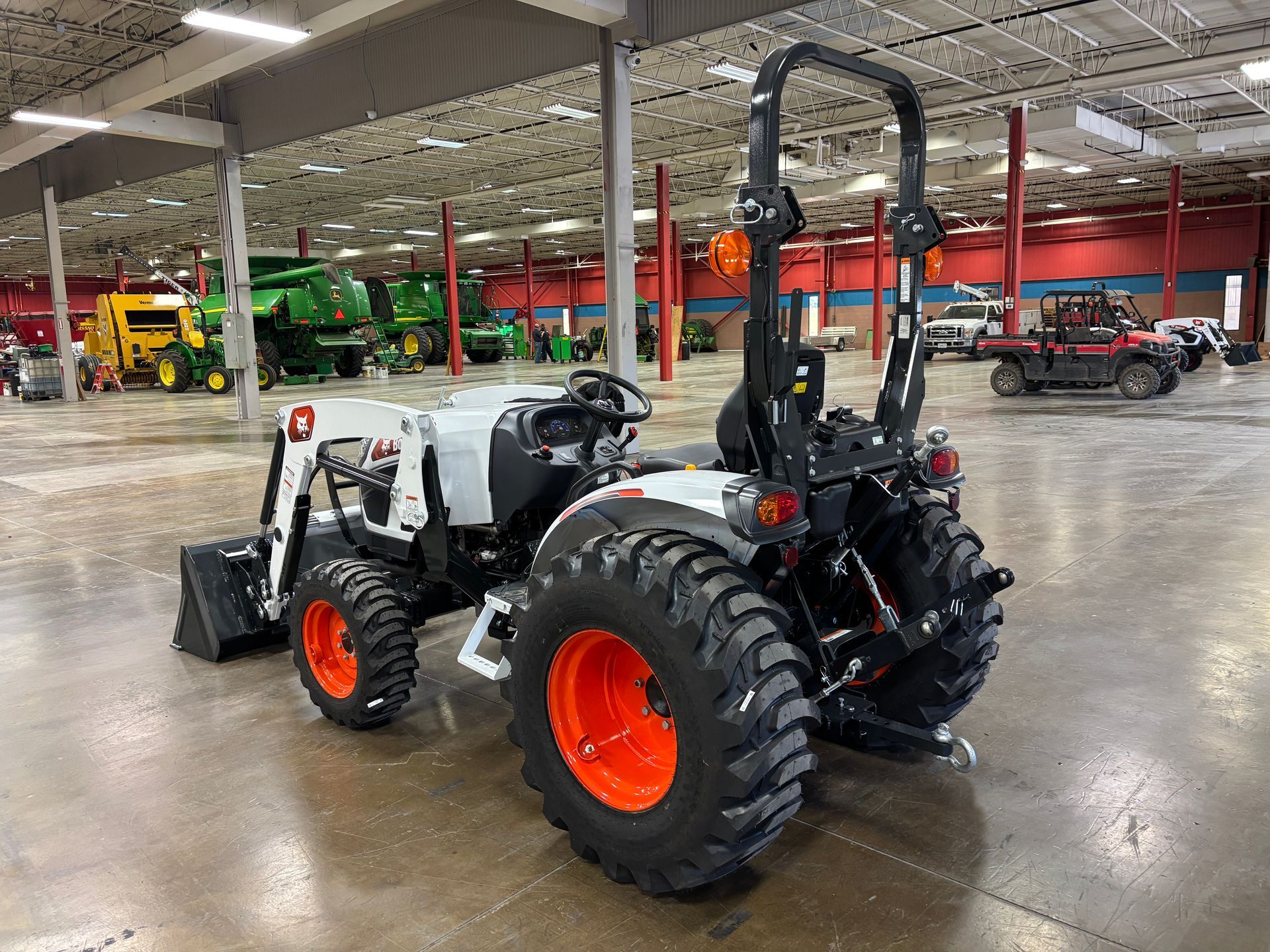 Bobcat tractor with orange wheels and black roll bar inside a large warehouse.