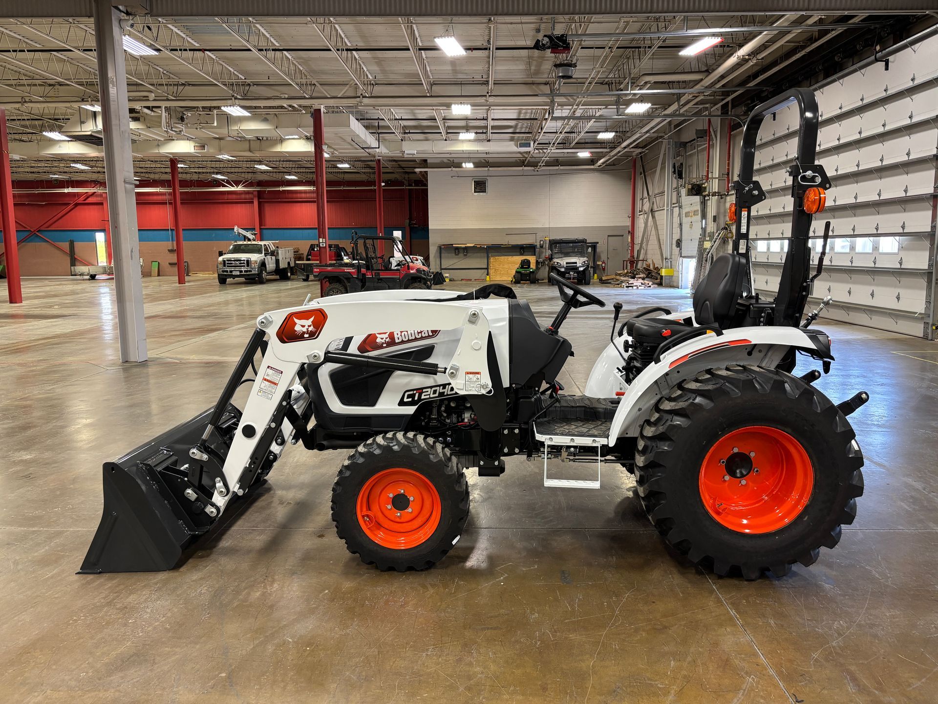 White Bobcat tractor with orange wheels and front loader, parked inside a warehouse.