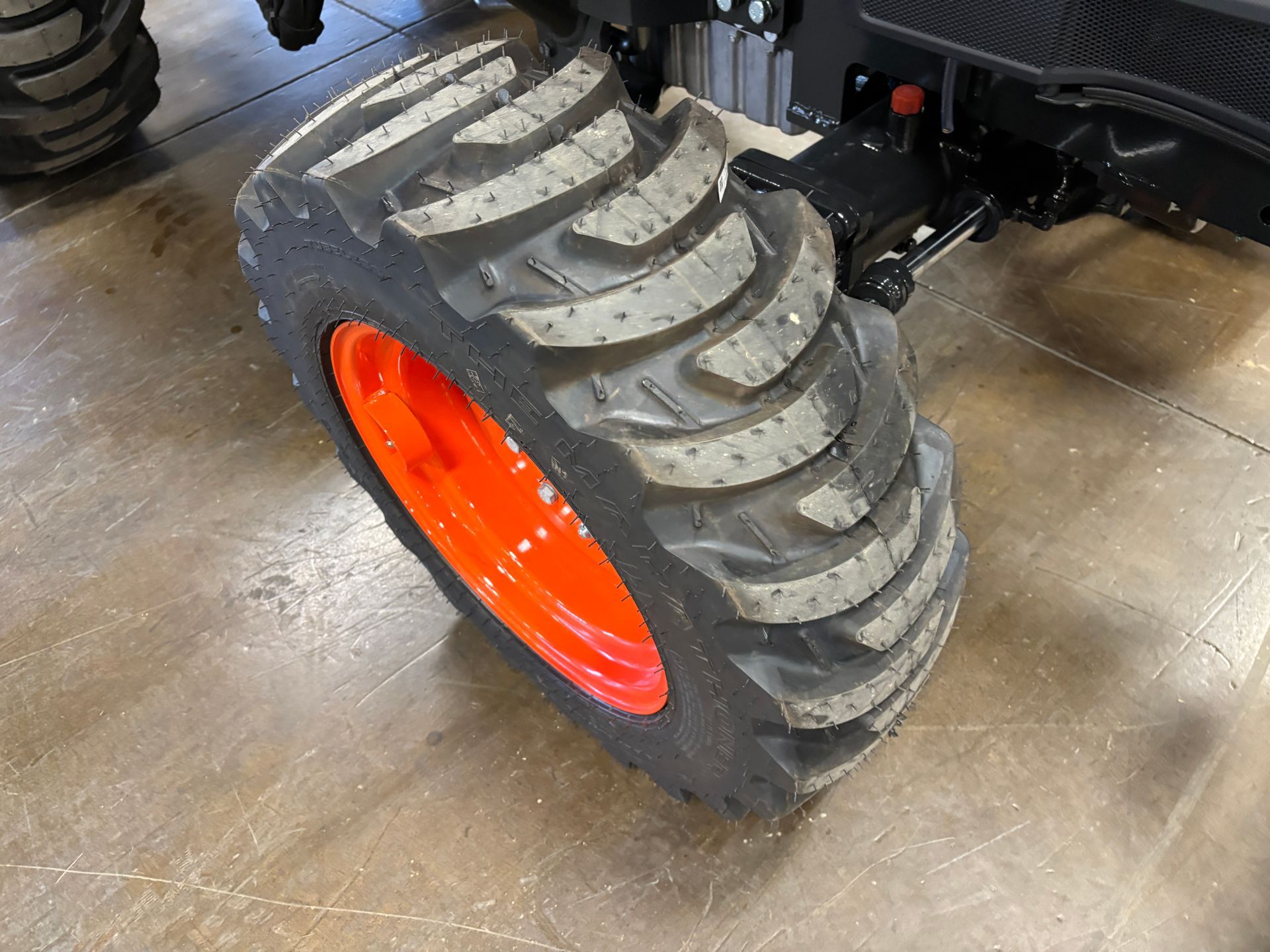 Orange tractor tire on a cement floor; black tire tread pattern; black tractor frame.
