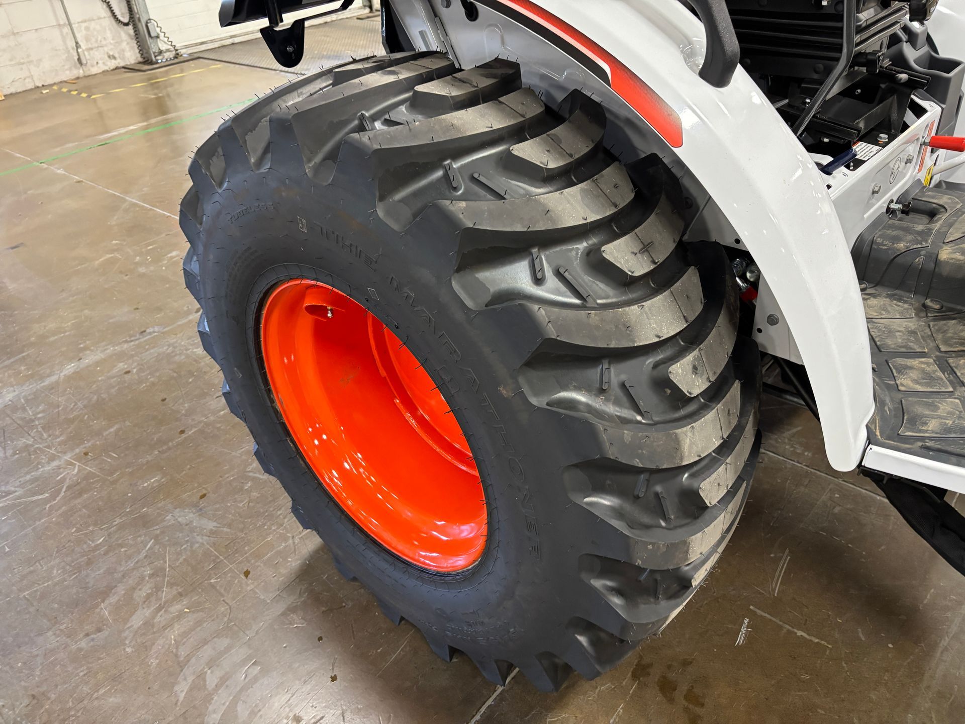 Tractor tire with black tread and orange rim. White tractor fender.
