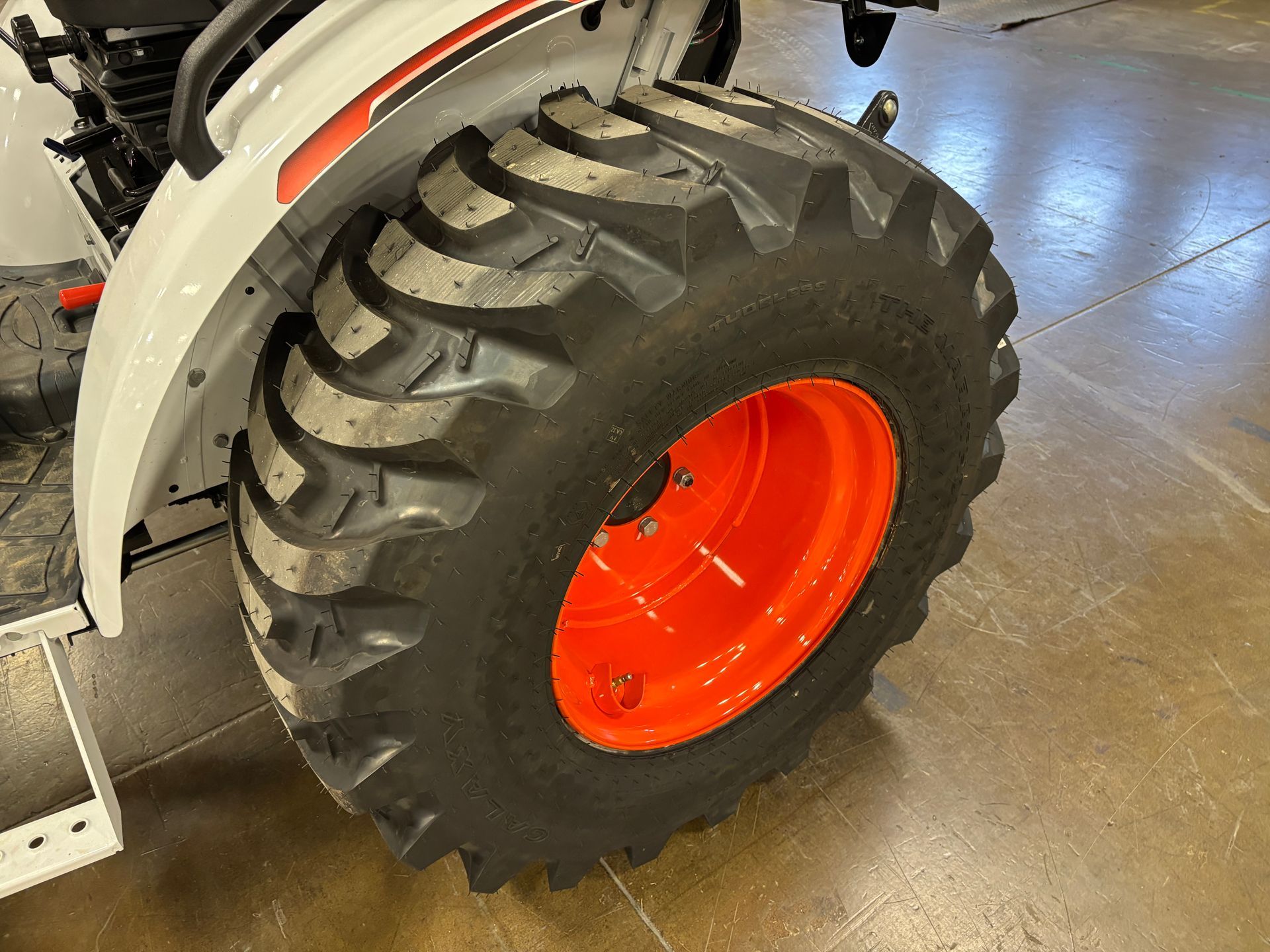 Tractor wheel with black tire and orange rim, white fender.