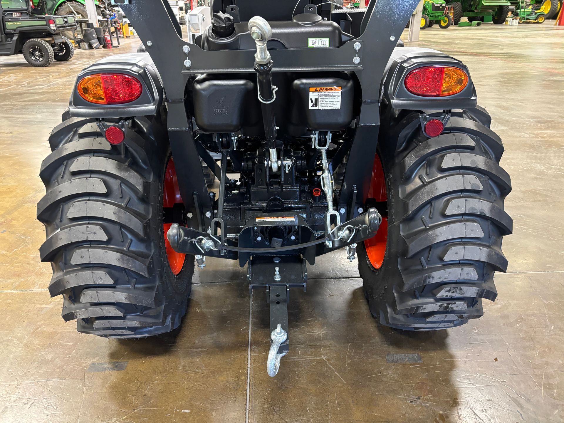 Rear view of a black tractor with large, black and orange tires. Tail lights and a hitch are visible.
