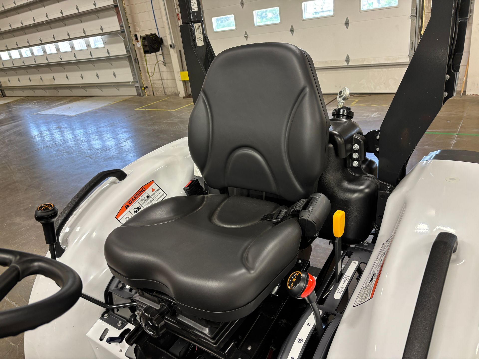 White tractor seat with black cushioning and armrest.
