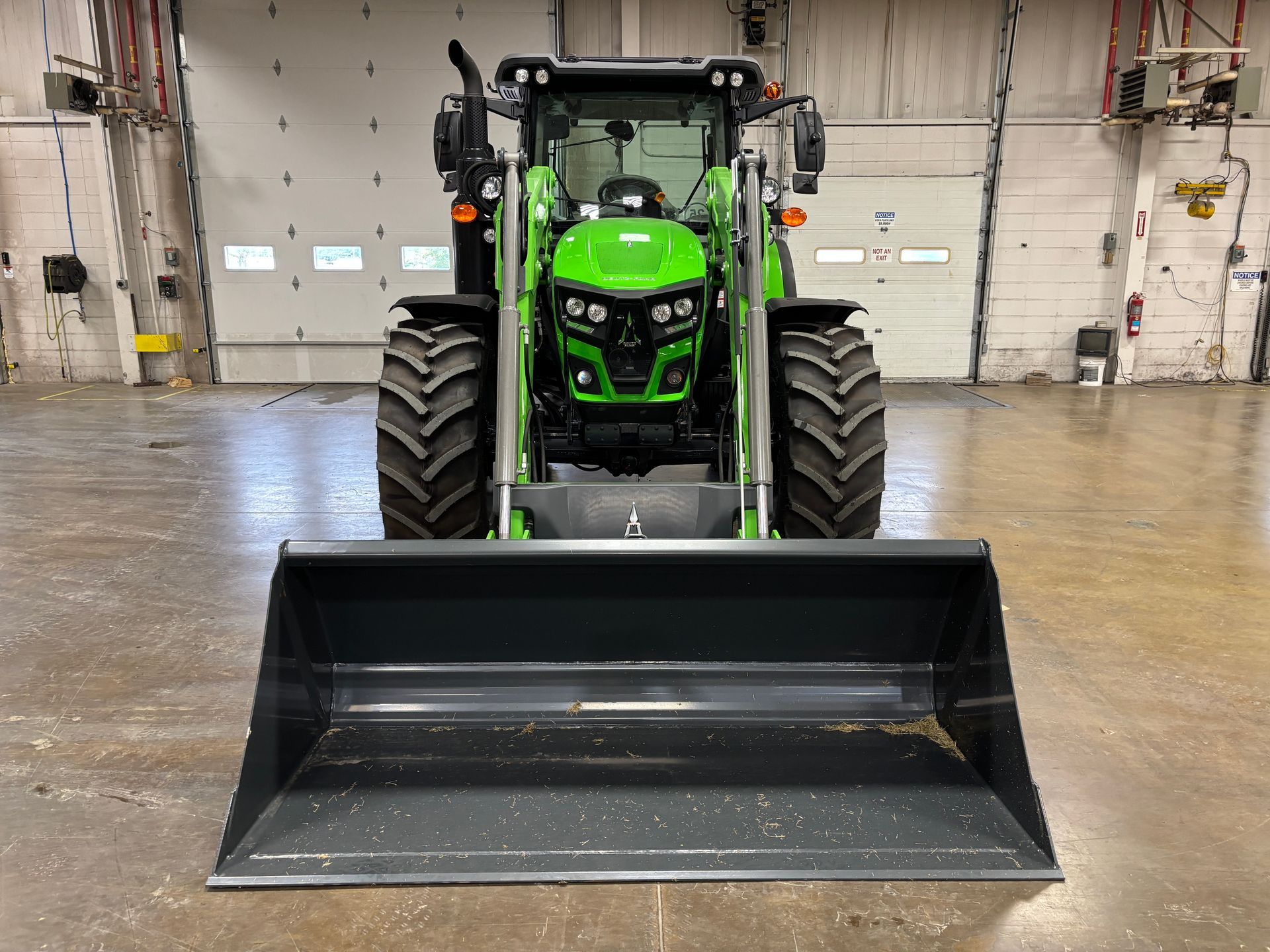Green and gray tractor with front-end loader in an industrial setting.