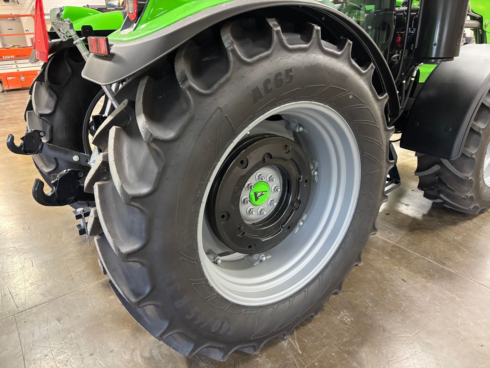 Close-up of a large tractor tire and wheel, with a green tractor in the background.