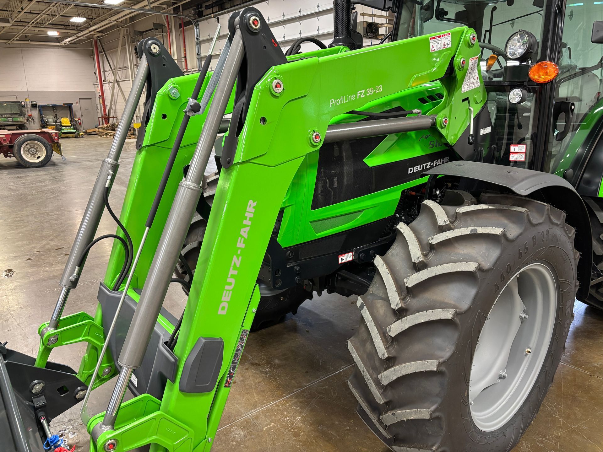 Green and black Deutz-Fahr tractor with front loader attachment parked inside a building.