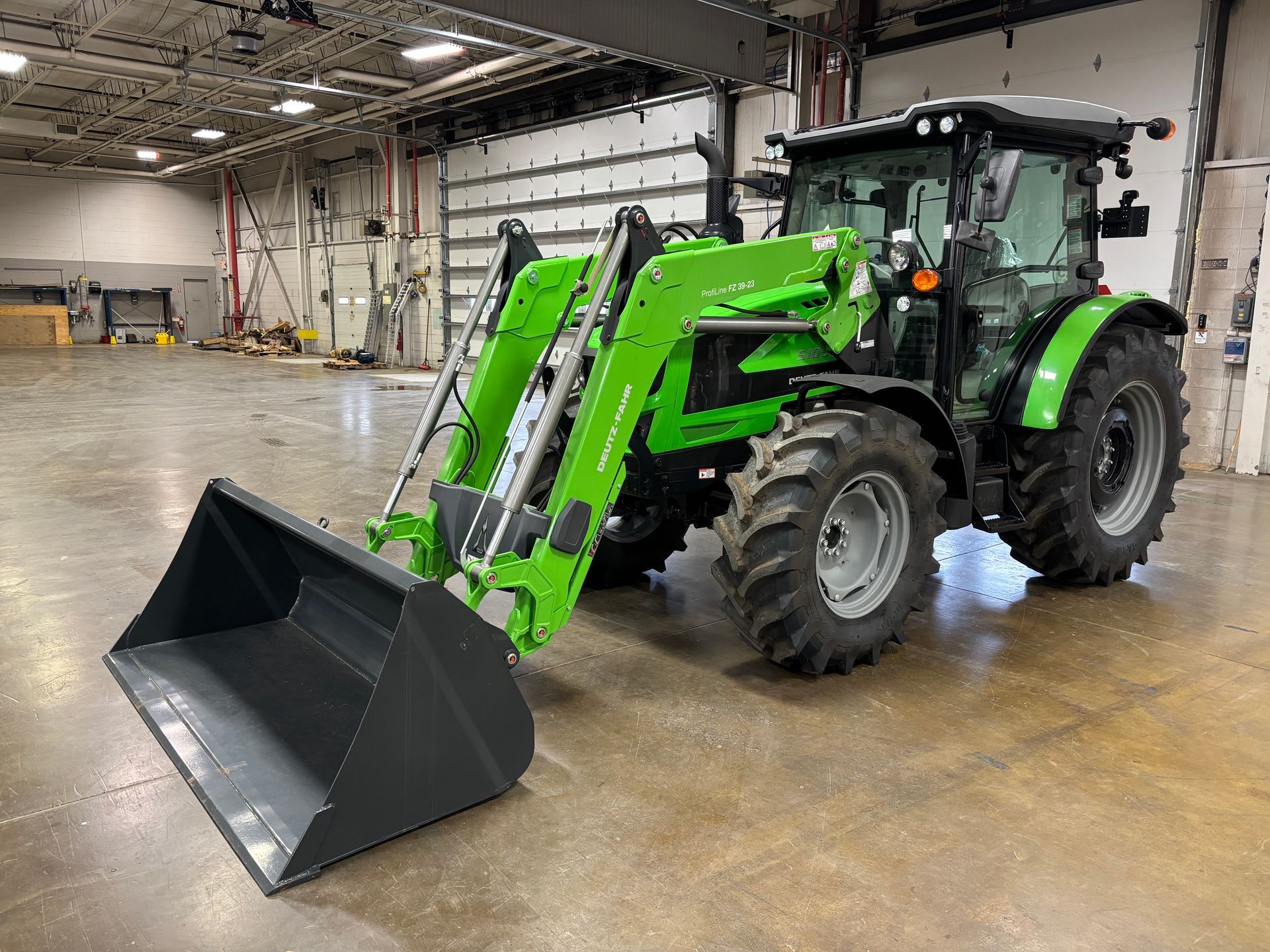 Green and black tractor with front loader in a warehouse setting.