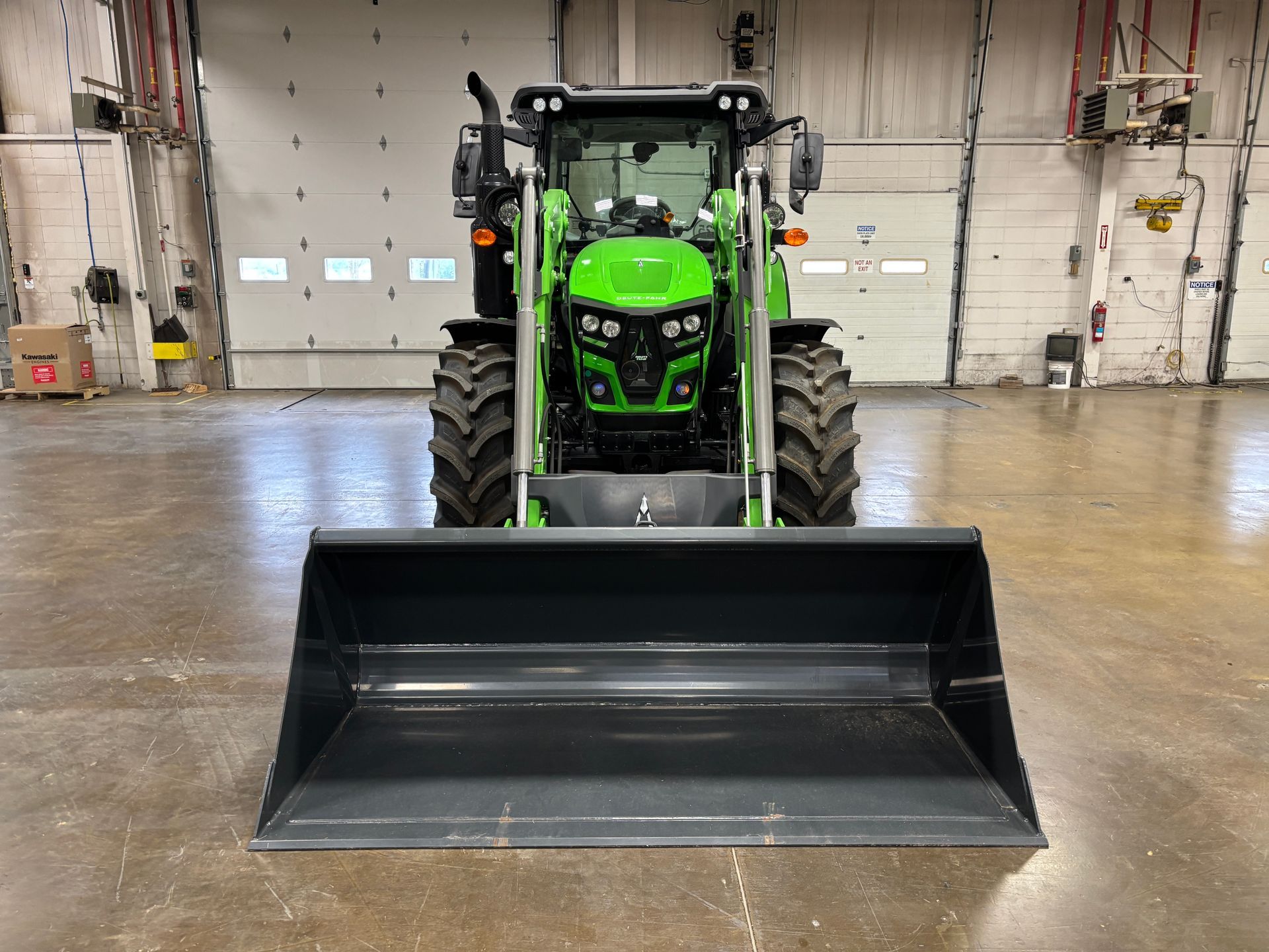 Green tractor with a front bucket parked inside a building.