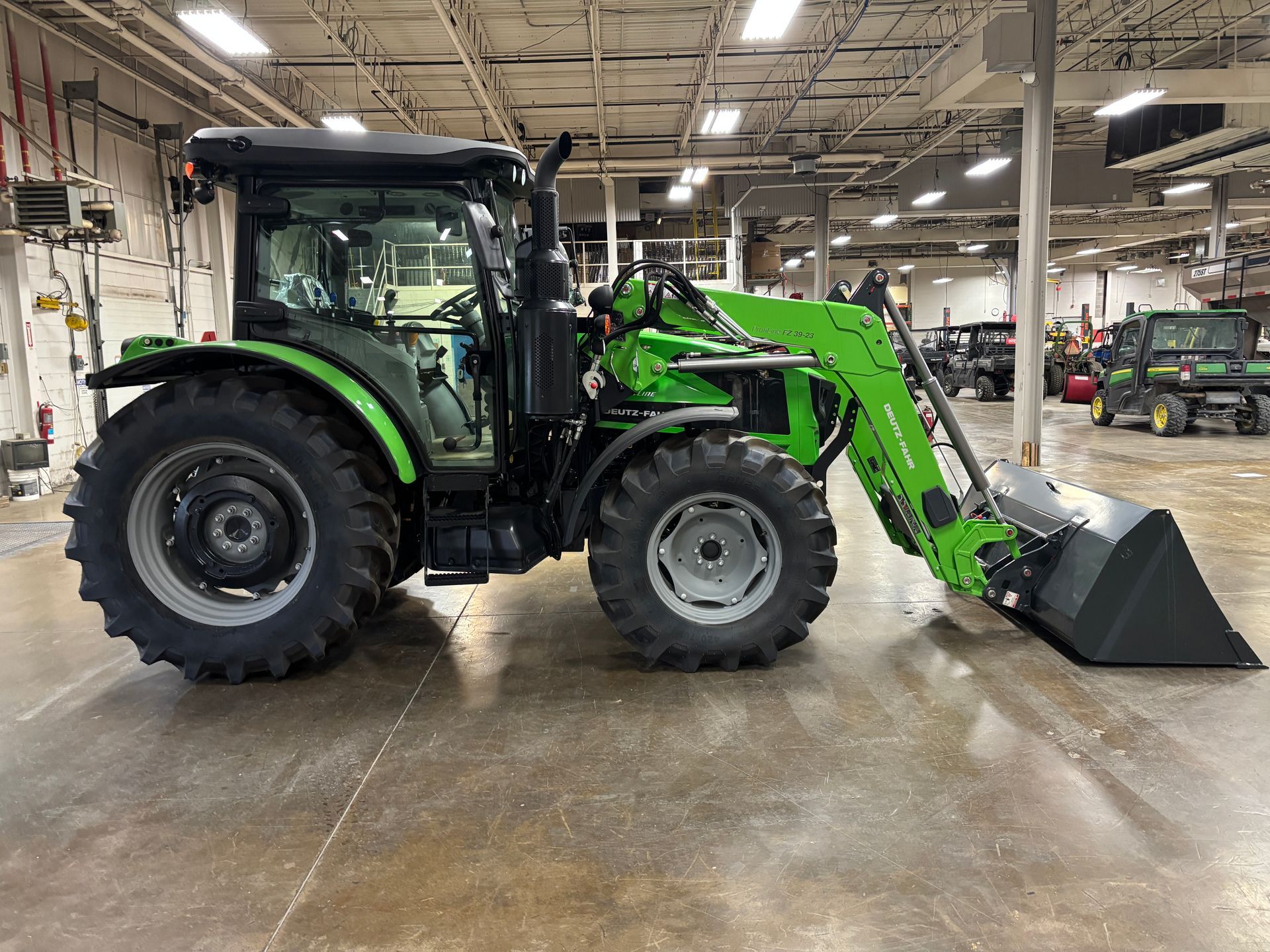 Green and black tractor with a front-end loader inside a large warehouse.