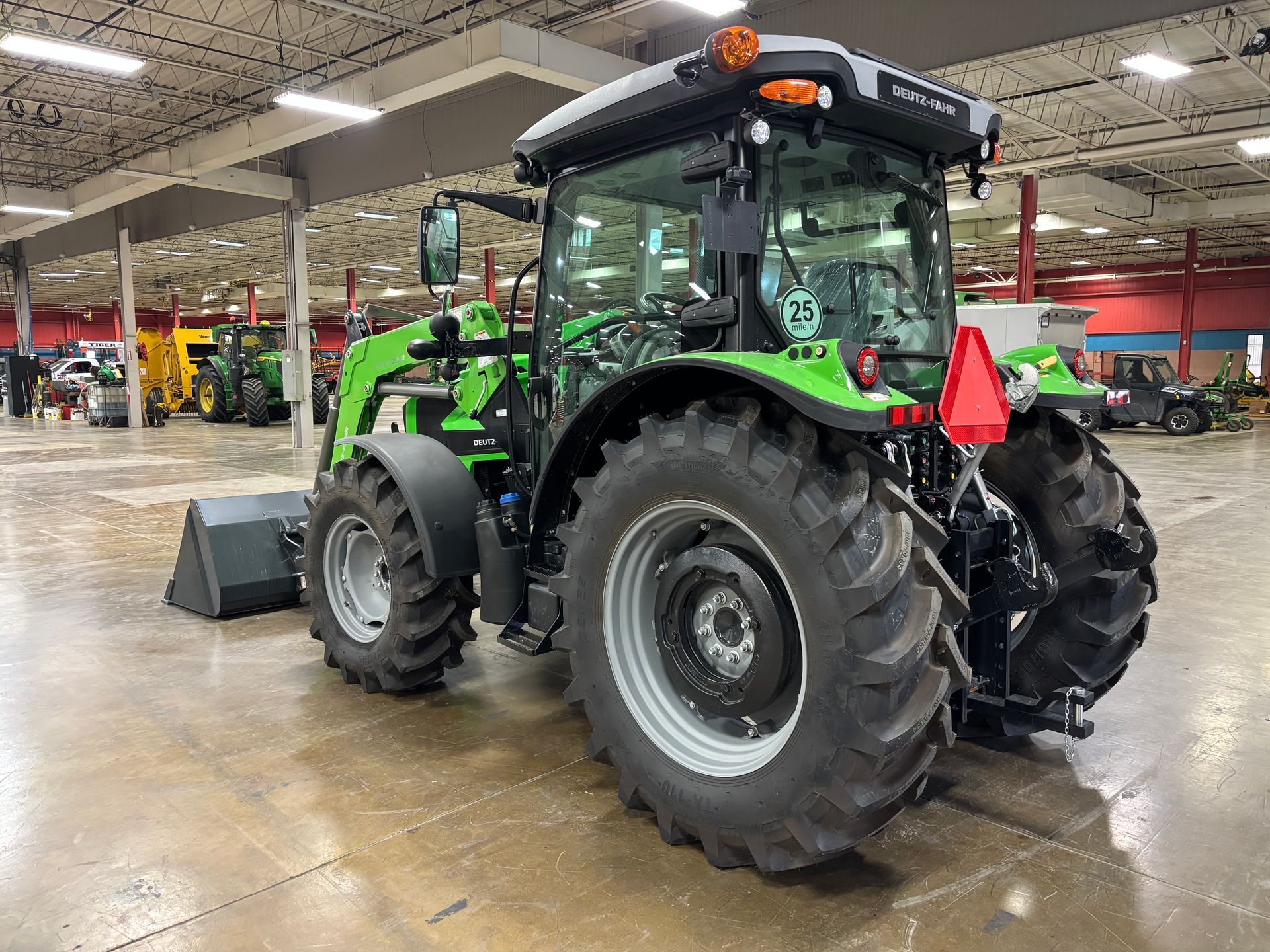 Green tractor inside a large building, with a front loader and a triangular red reflector.