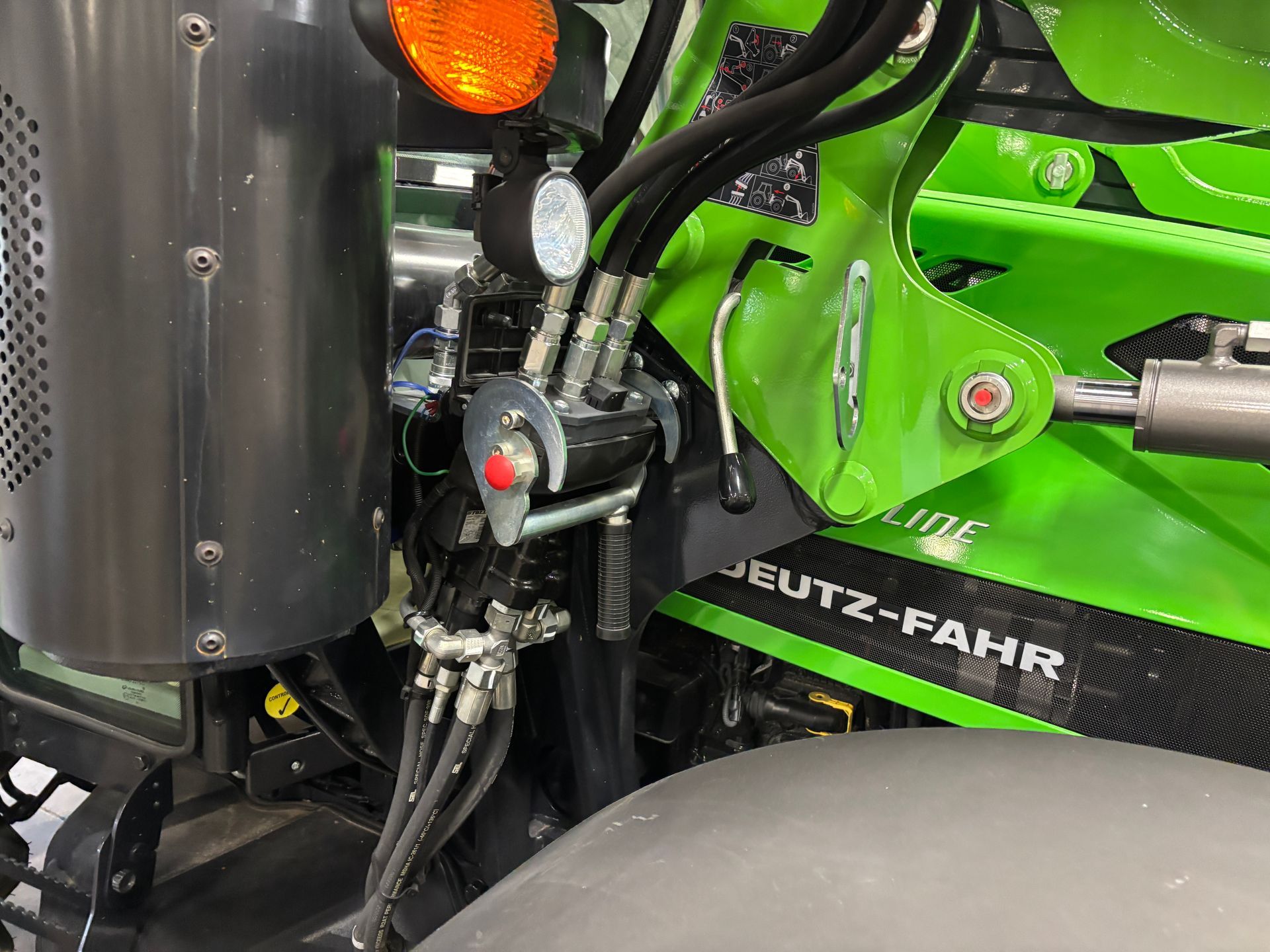 Close-up of tractor hydraulics with black hoses, a red button, and DEUTZ-FAHR branding in green and black.