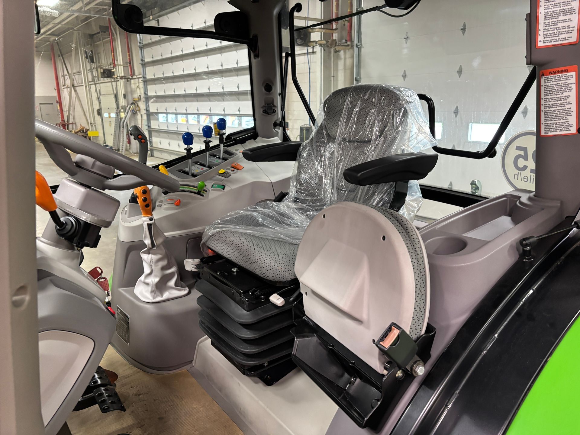 Interior of a tractor cab: grey seat, controls, levers. Plastic seat cover.