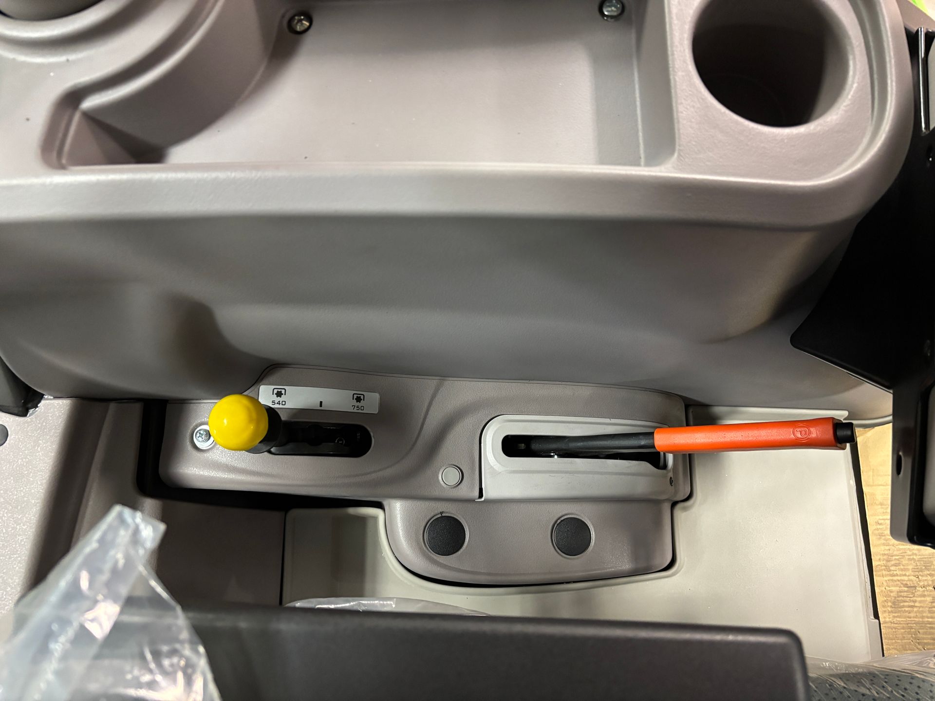 Interior of a tractor's cab; gray console with a yellow lever, a slot with an orange handle, and cup holder.