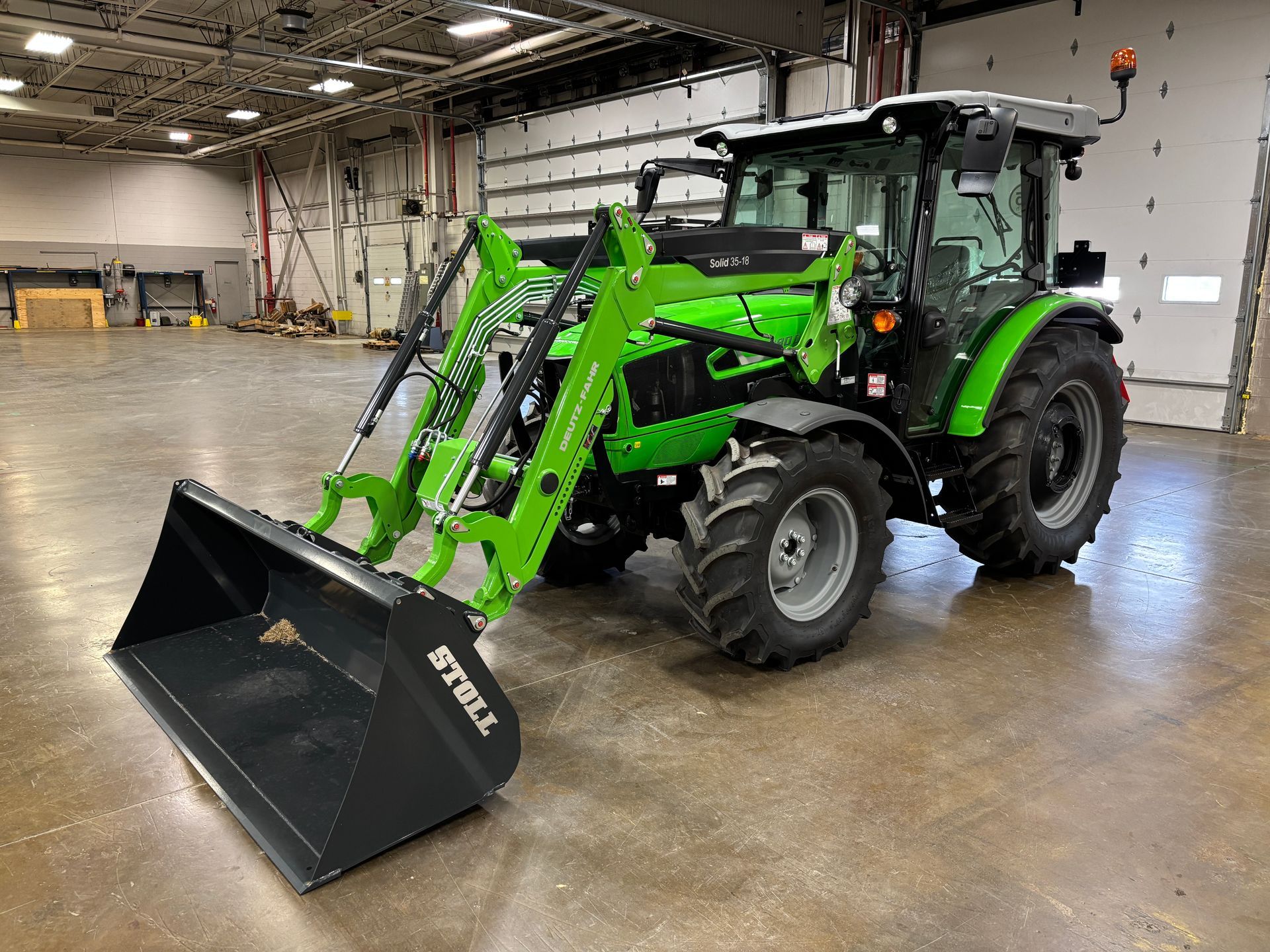 Green and black Deutz-Fahr tractor with a front loader and bucket parked inside a large warehouse.
