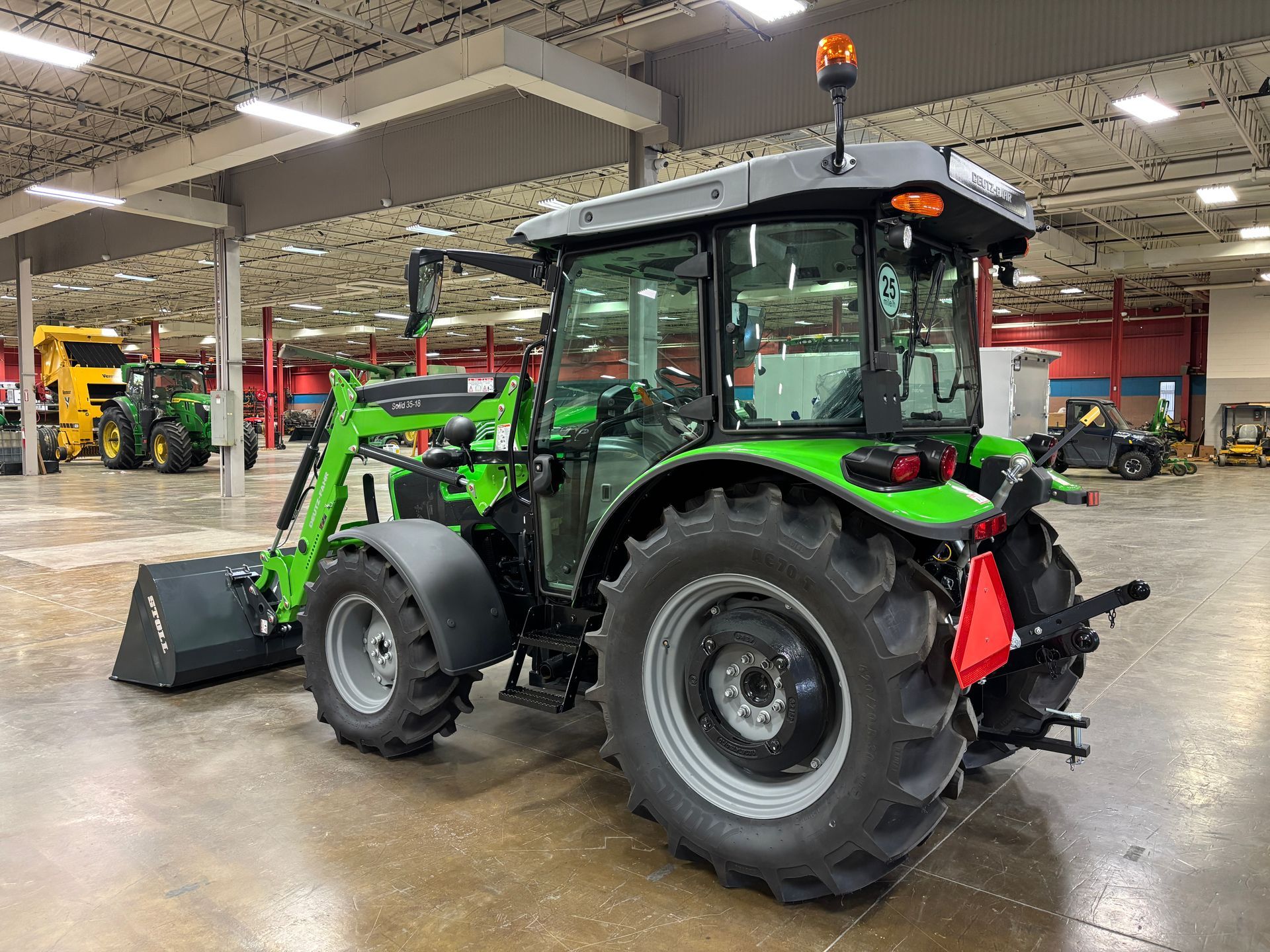Green tractor with front loader inside a warehouse.