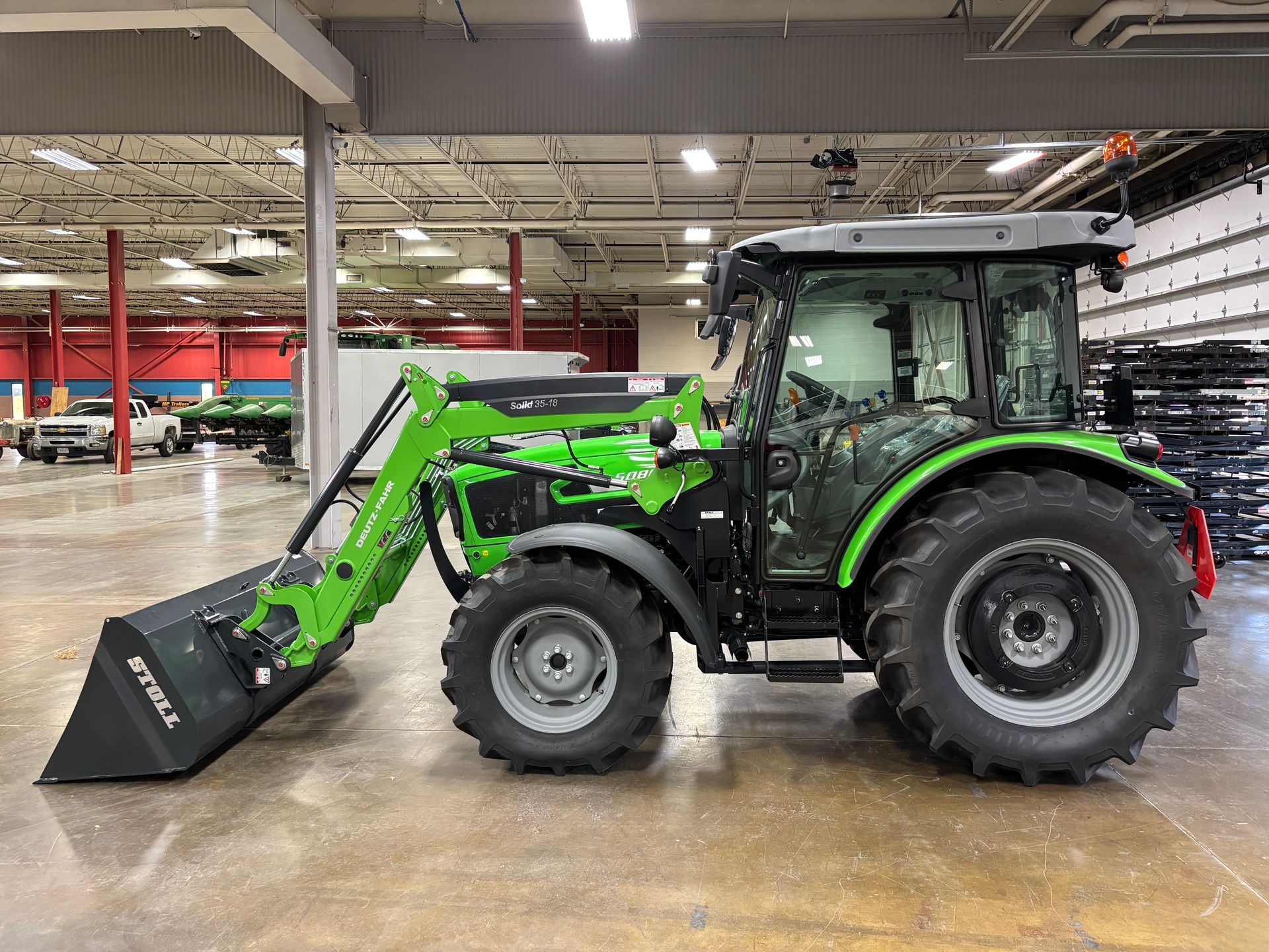 Green and gray tractor with front loader inside a building.