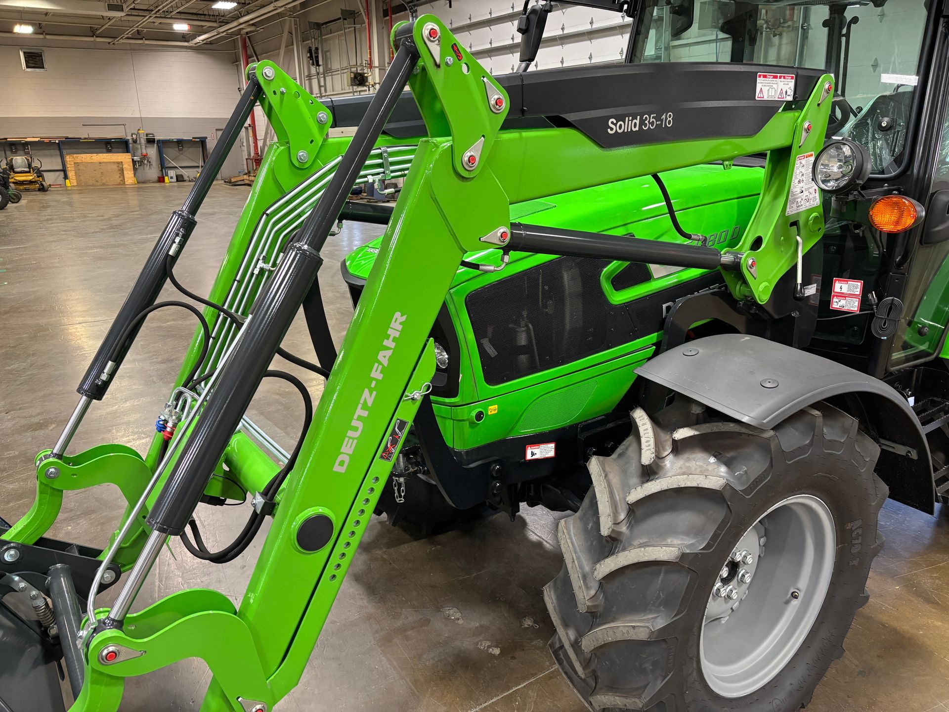 Green Deutz-Fahr tractor with a front loader; indoors with a gray wheel, black tires, and shiny green paint.
