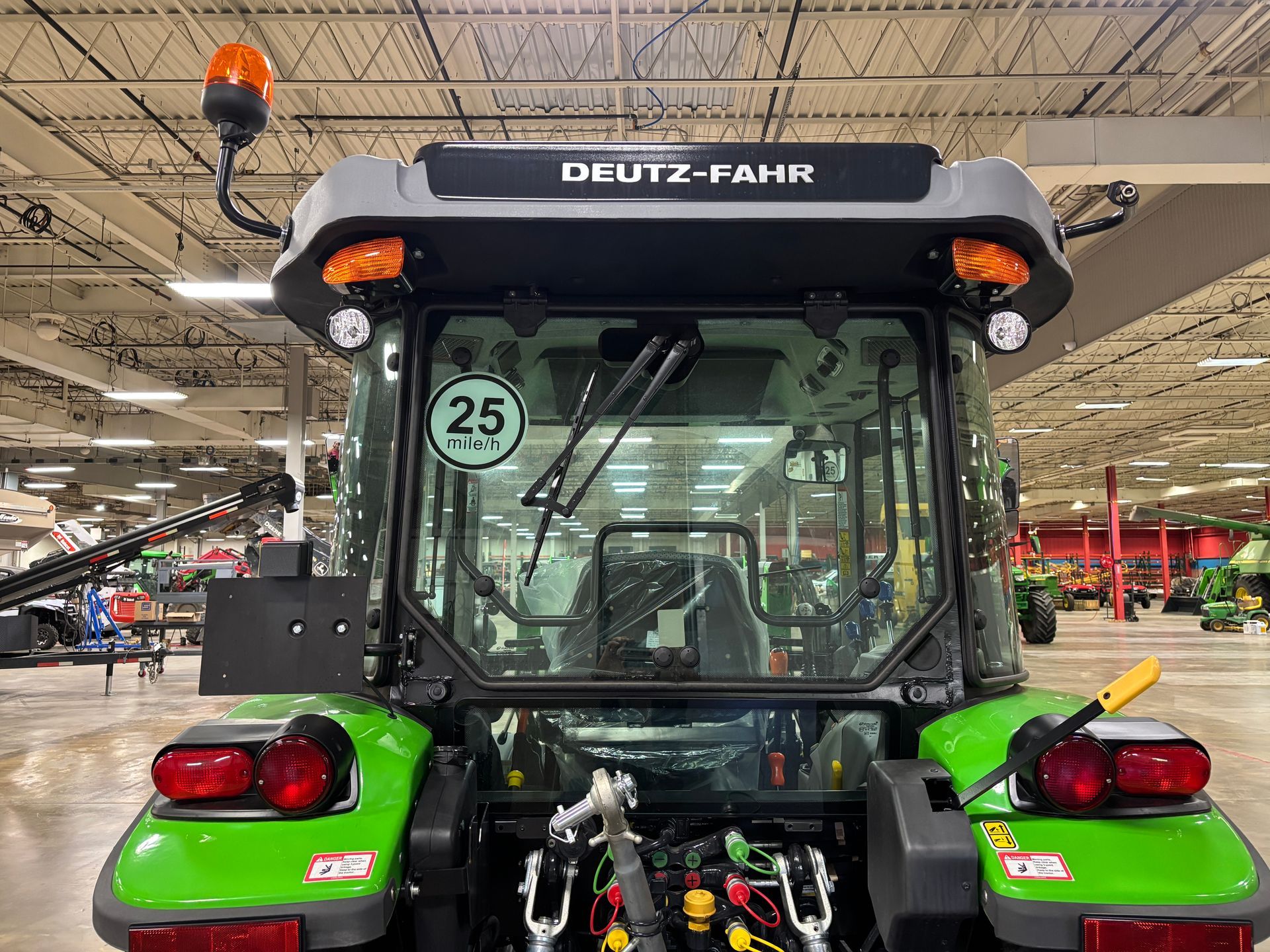 Rear view of a green and gray Deutz-Fahr tractor in a showroom, with flashing lights and a speed sign.