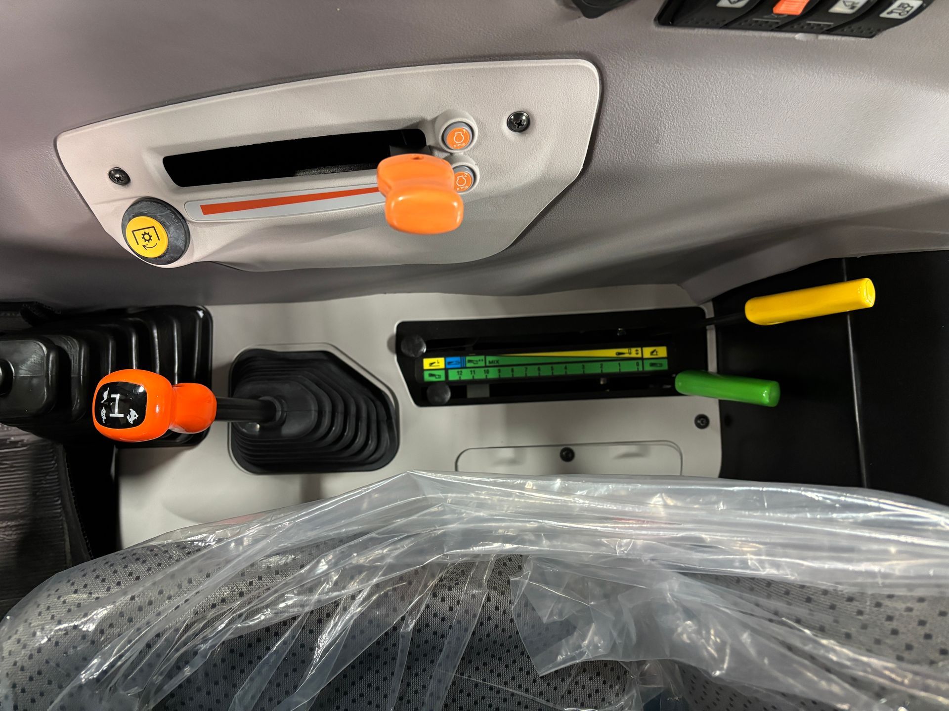 Interior view of tractor controls: levers, gauges, and a gear shift. Orange, yellow, and green accents.