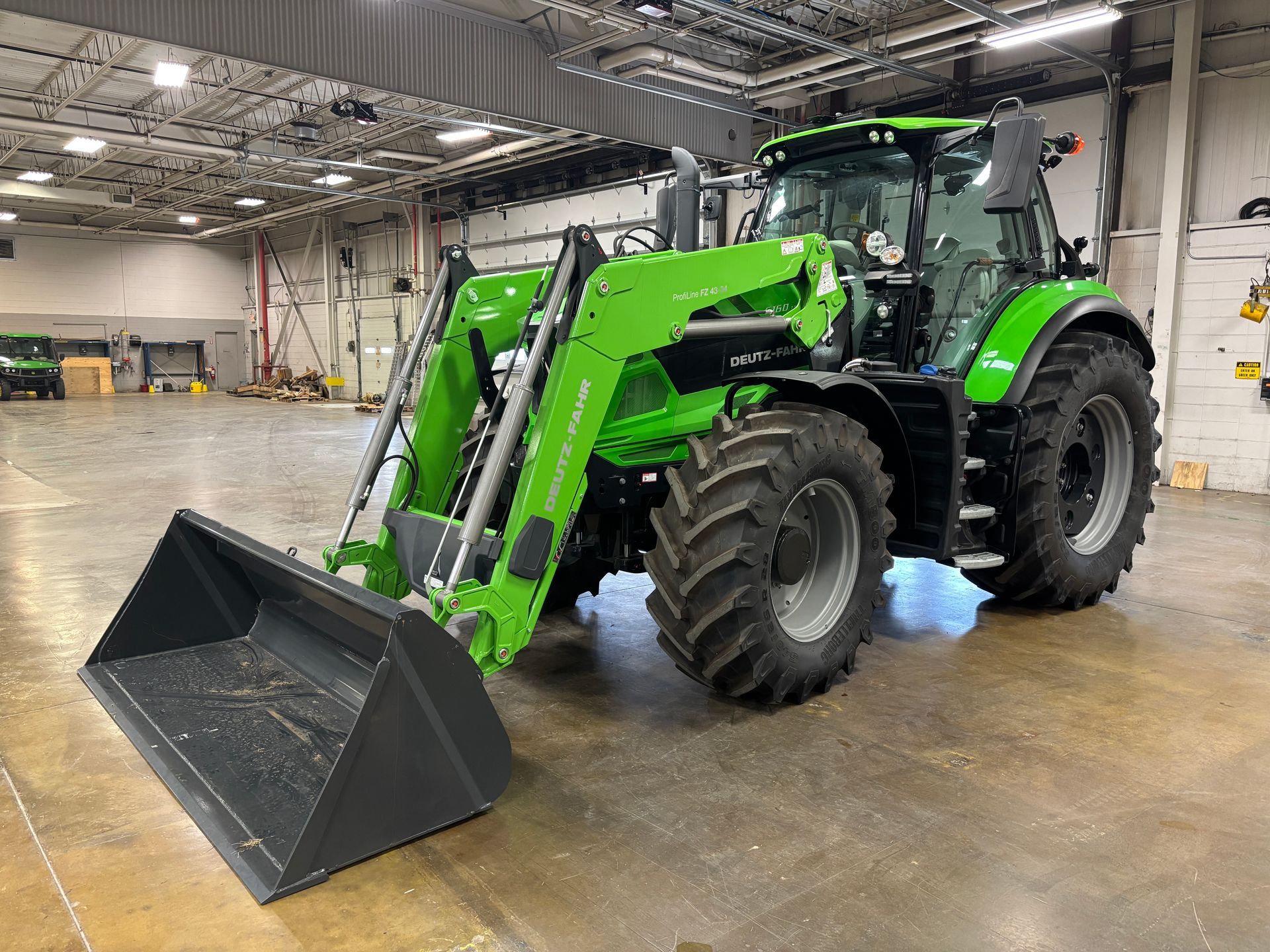 Green tractor with front loader inside a warehouse.