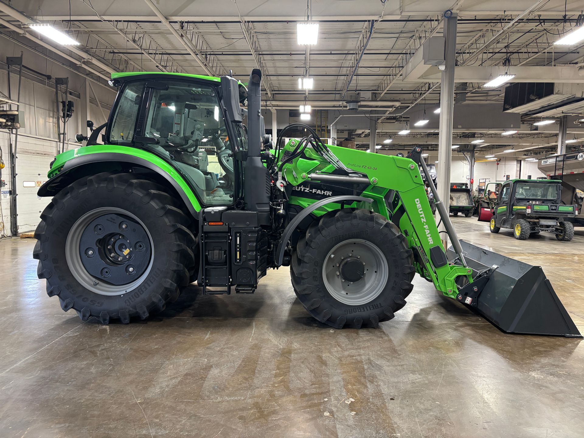 Green tractor with loader bucket, parked indoors on a concrete floor.
