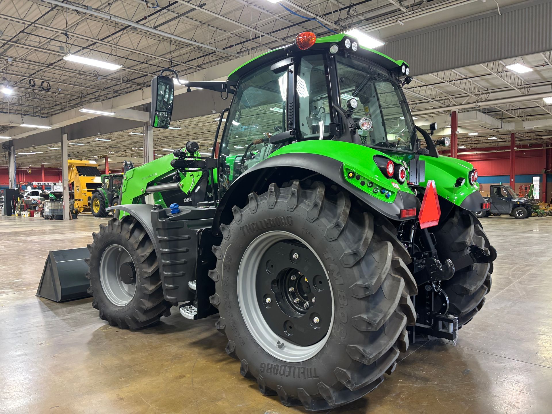 Green tractor with large tires, parked in a showroom.