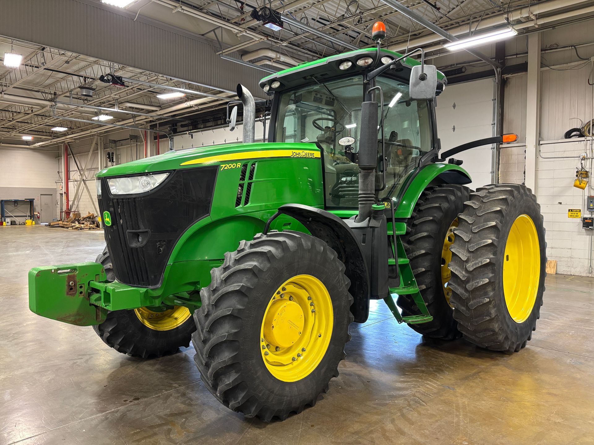 Green John Deere tractor with large tires on a concrete floor inside a building.
