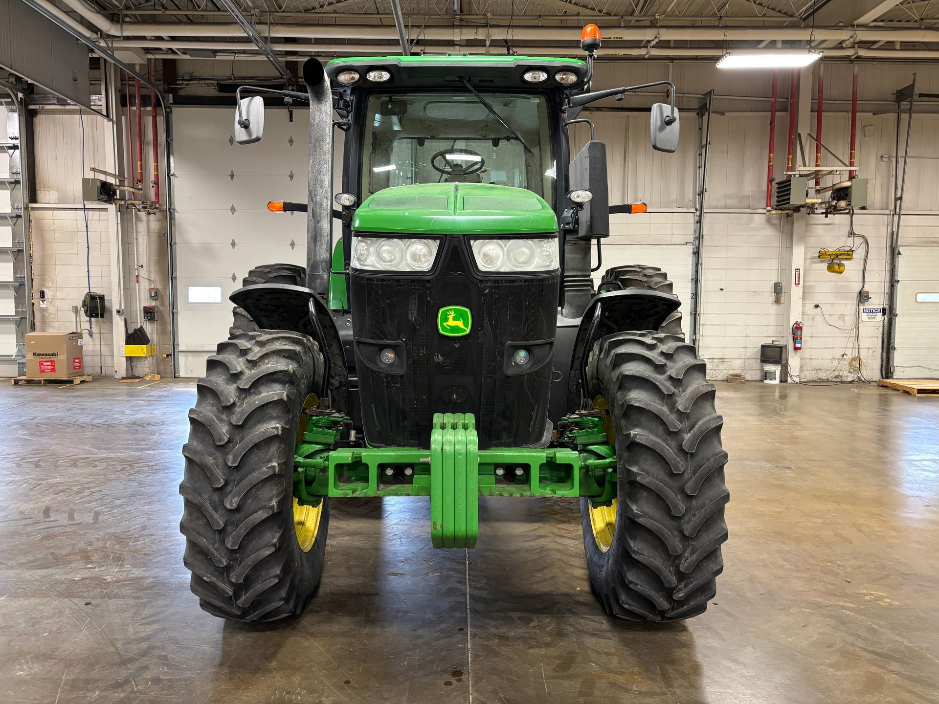 Green John Deere tractor, front view, in a warehouse setting.