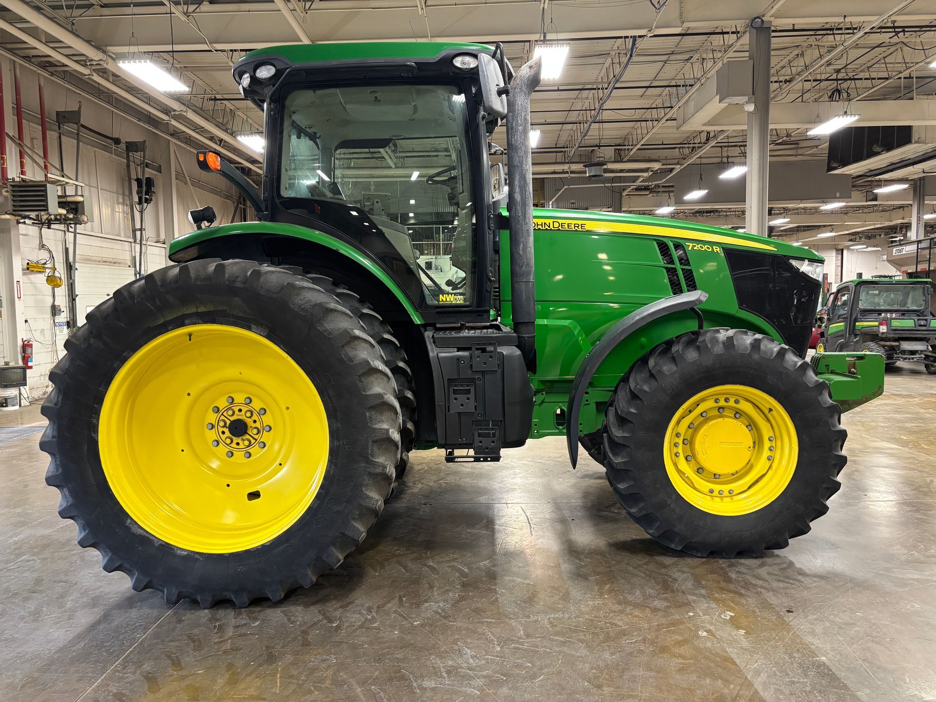 John Deere green and yellow tractor with a cab, parked indoors.