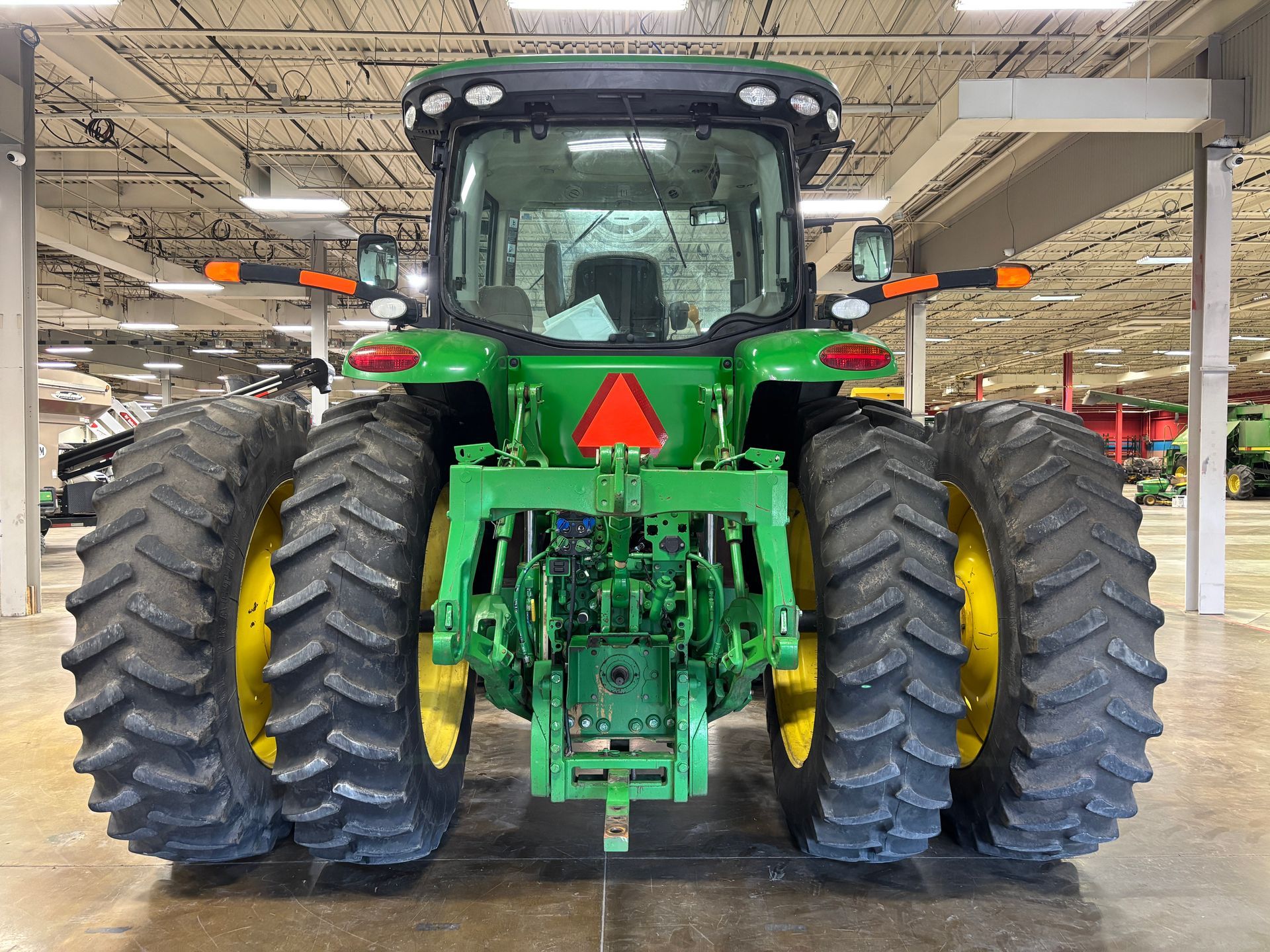 Rear view of a green and yellow John Deere tractor, large tires, indoor setting.