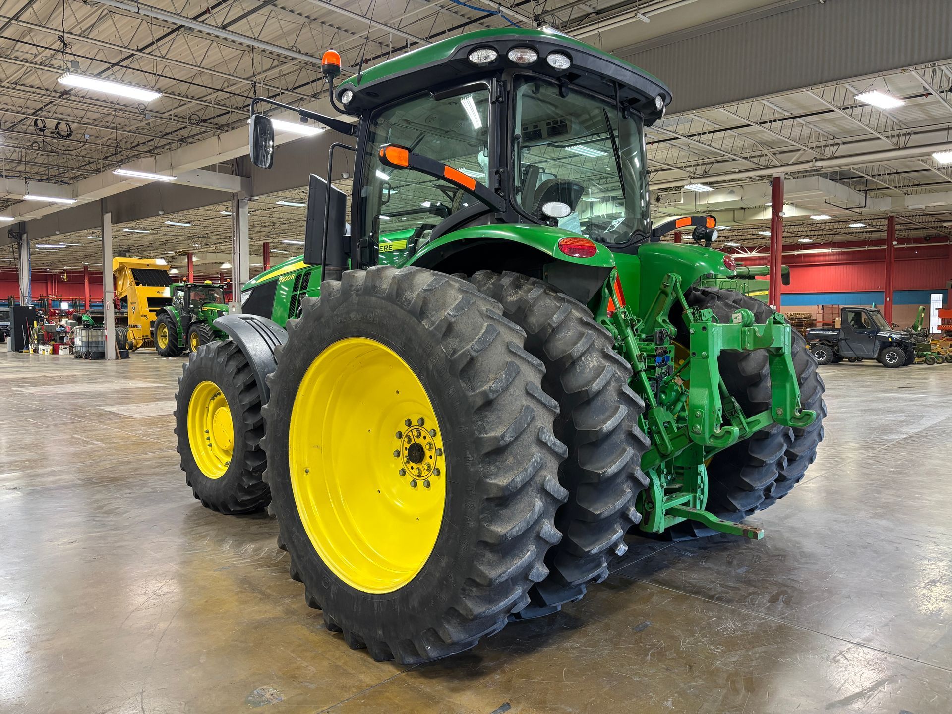 Green John Deere tractor with large tires on display in a large building.