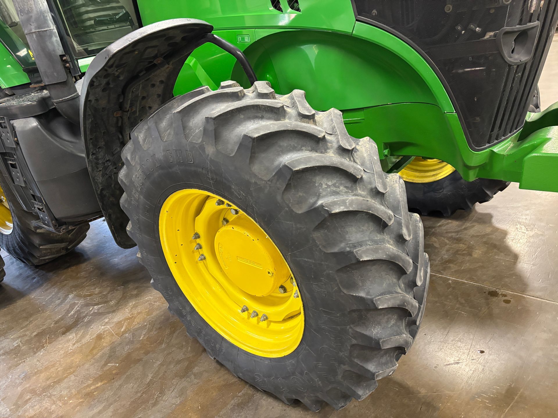 Green John Deere tractor tire, yellow wheel, on a concrete floor.