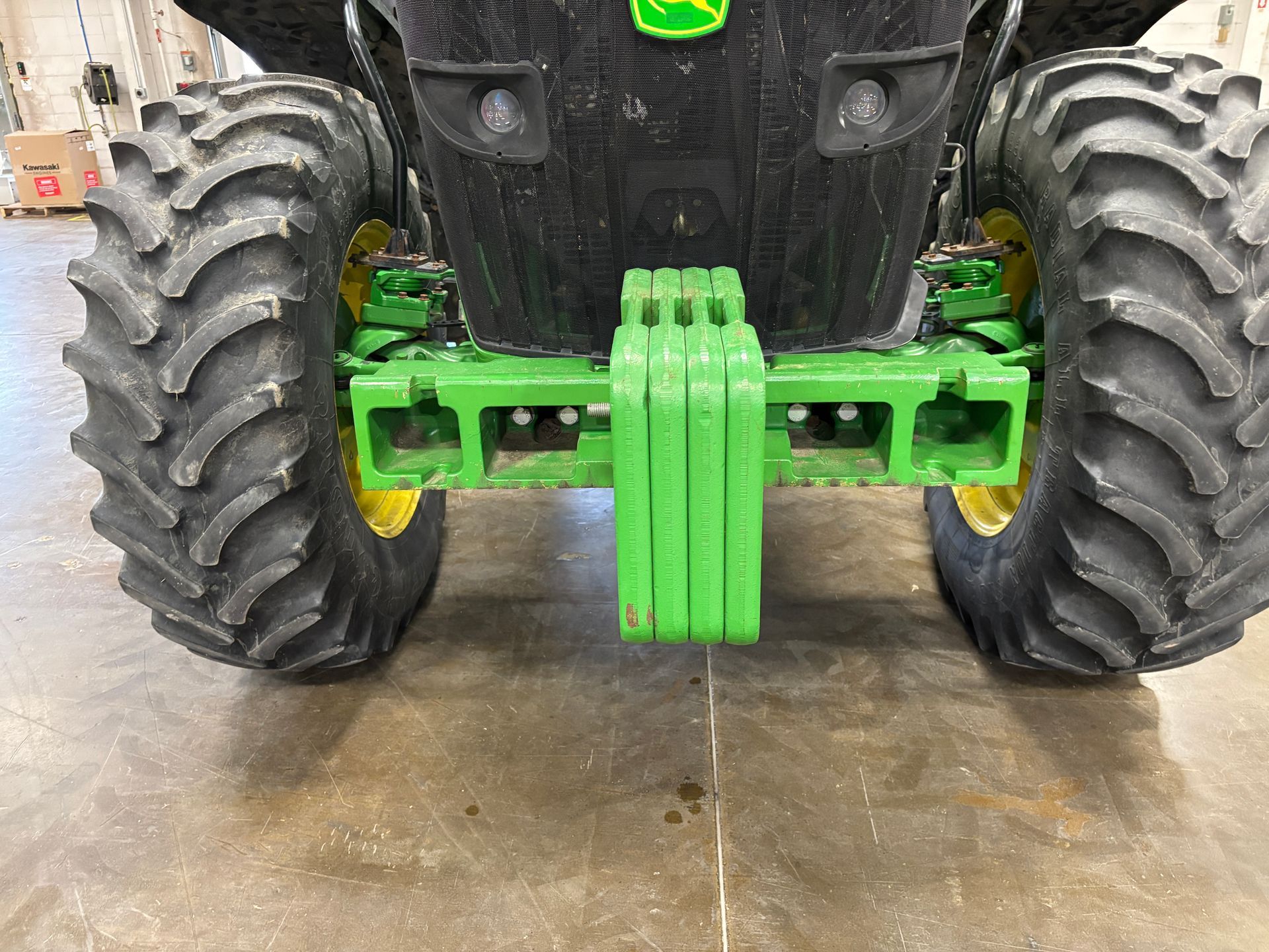 Green and black John Deere tractor rear with large tires and front weight.