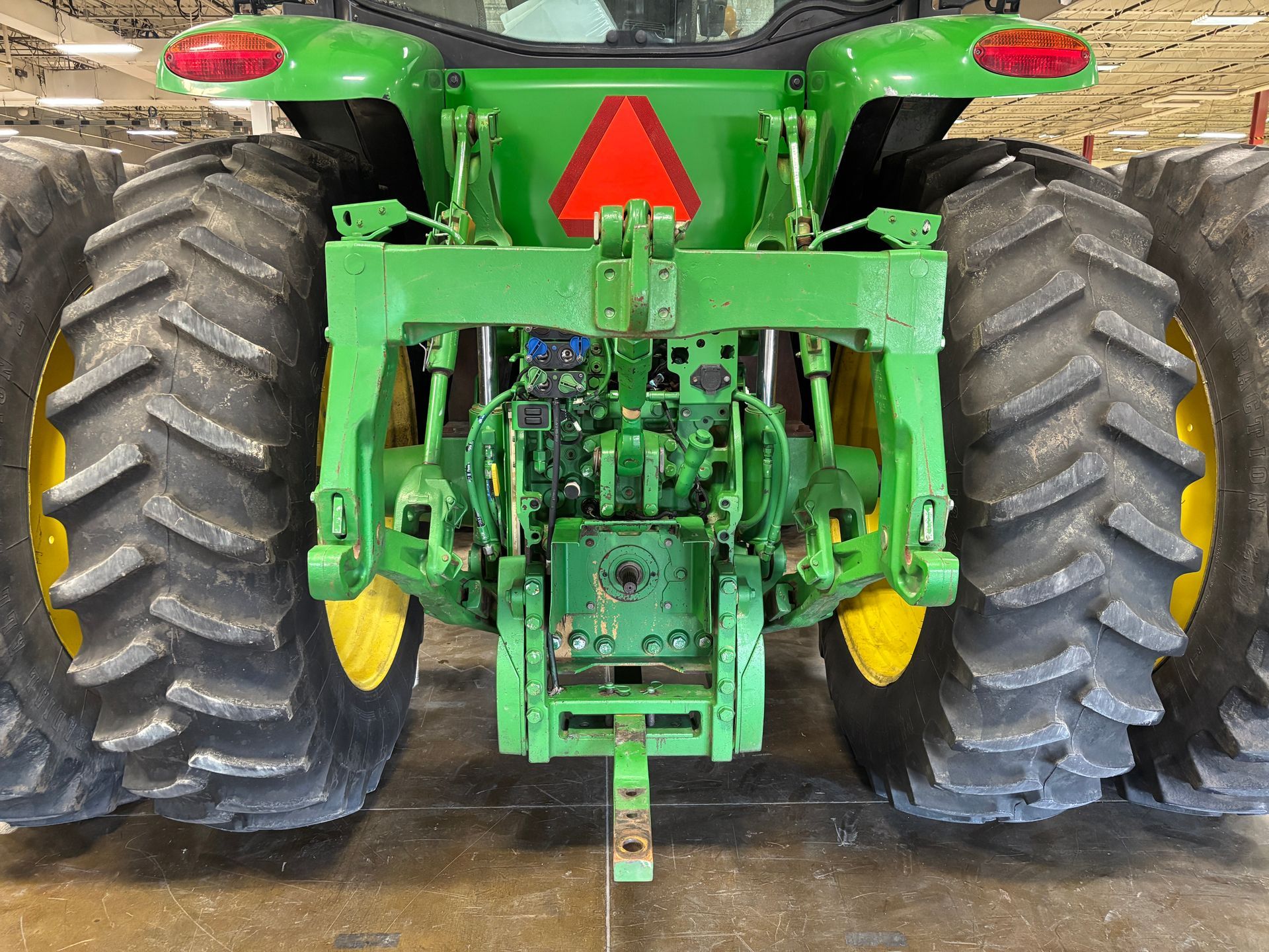 Rear view of a green John Deere tractor with large tires, a hitch, and a red triangle warning.