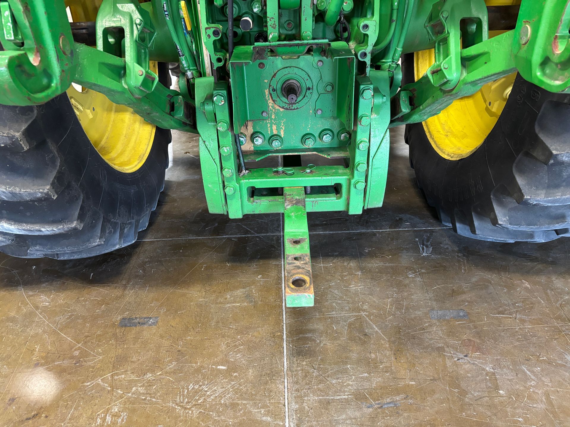 Rear view of a green and yellow tractor with a hitch, parked on a concrete floor.