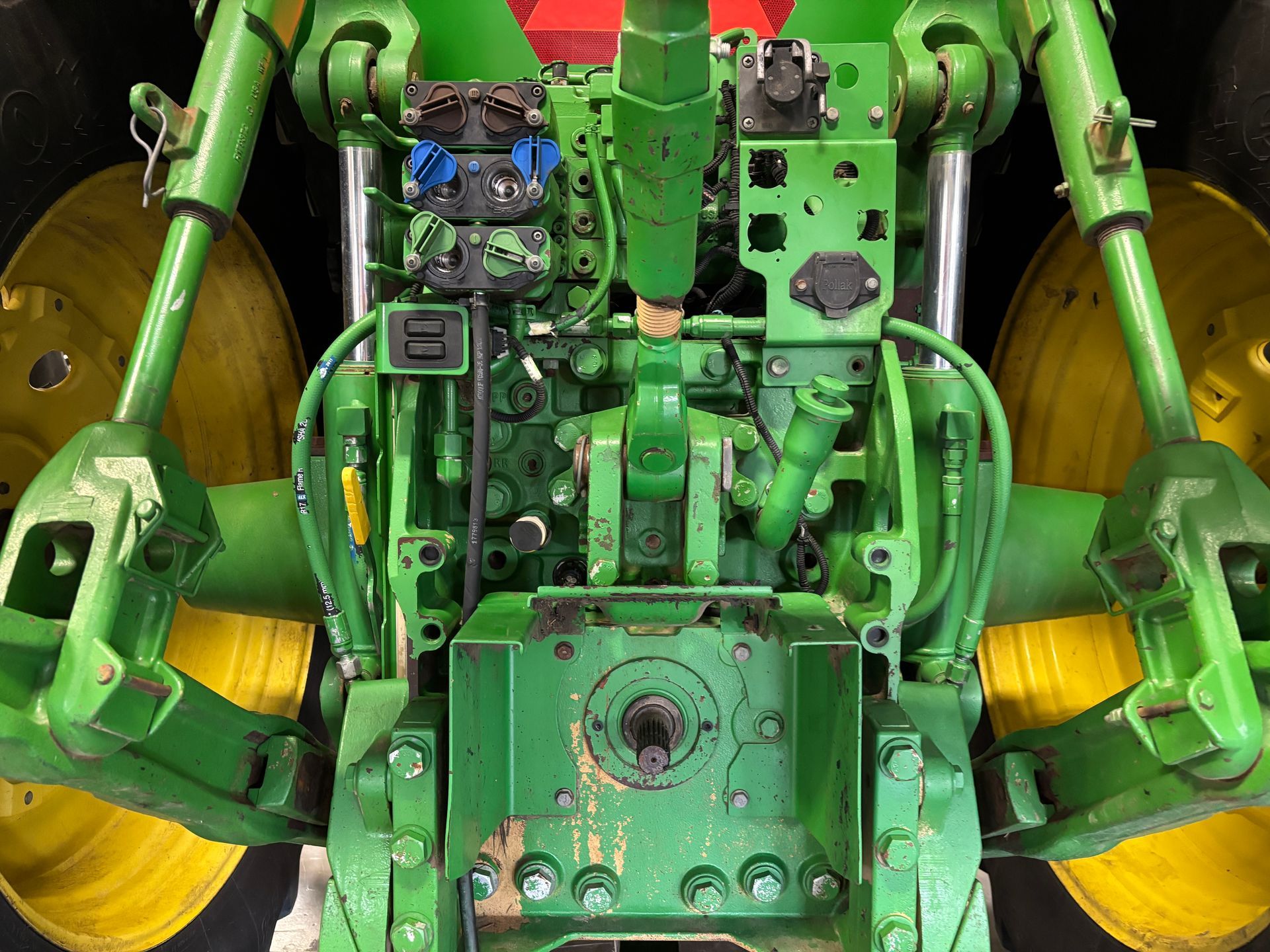 Green and yellow tractor's rear with wheels visible. Mechanical components and hydraulic lines are featured prominently.