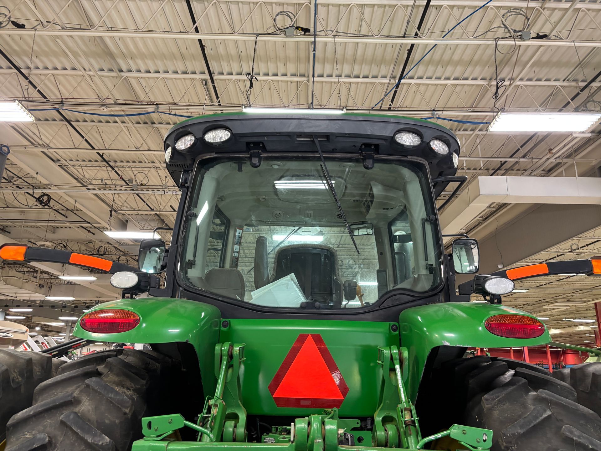 Green John Deere tractor rear view, cab with lights, inside a building.