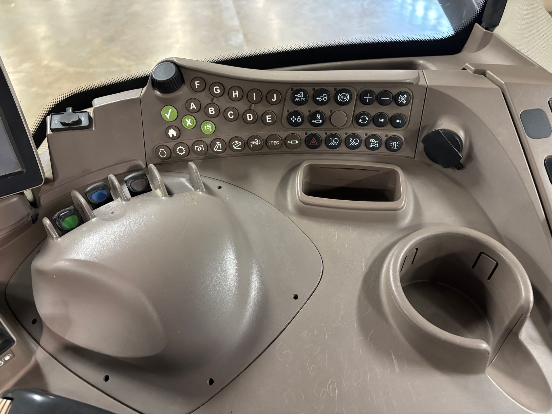 Dashboard of an agricultural machine, beige with buttons, levers, a cup holder, and a display screen.