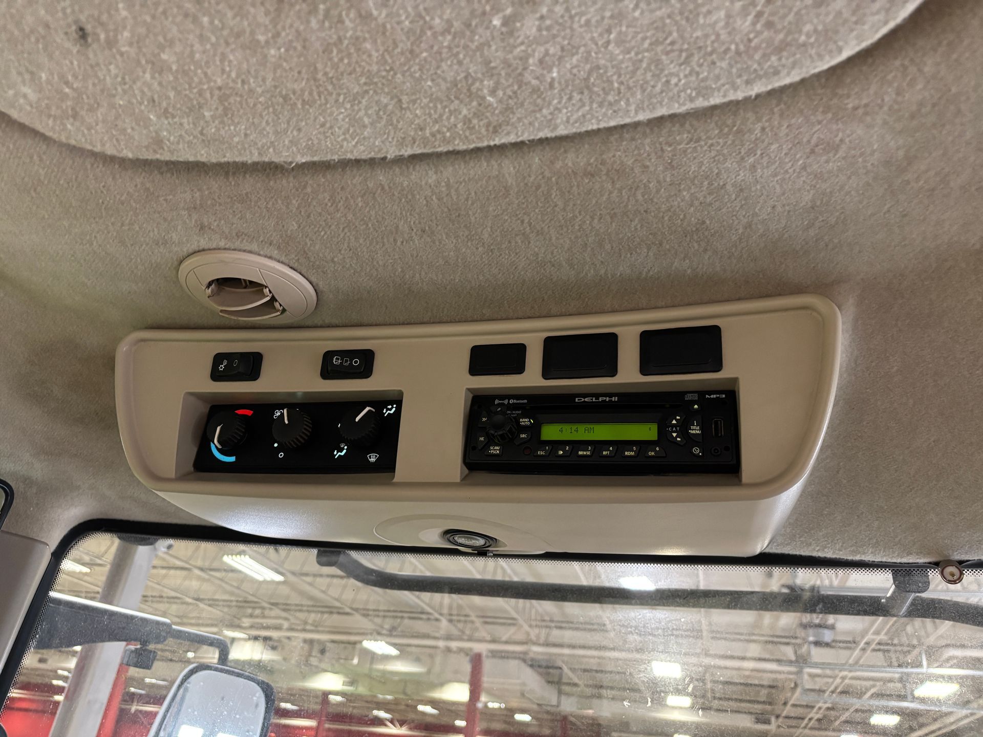 Interior cab of a vehicle showing an air conditioning control panel and radio mounted in the ceiling.