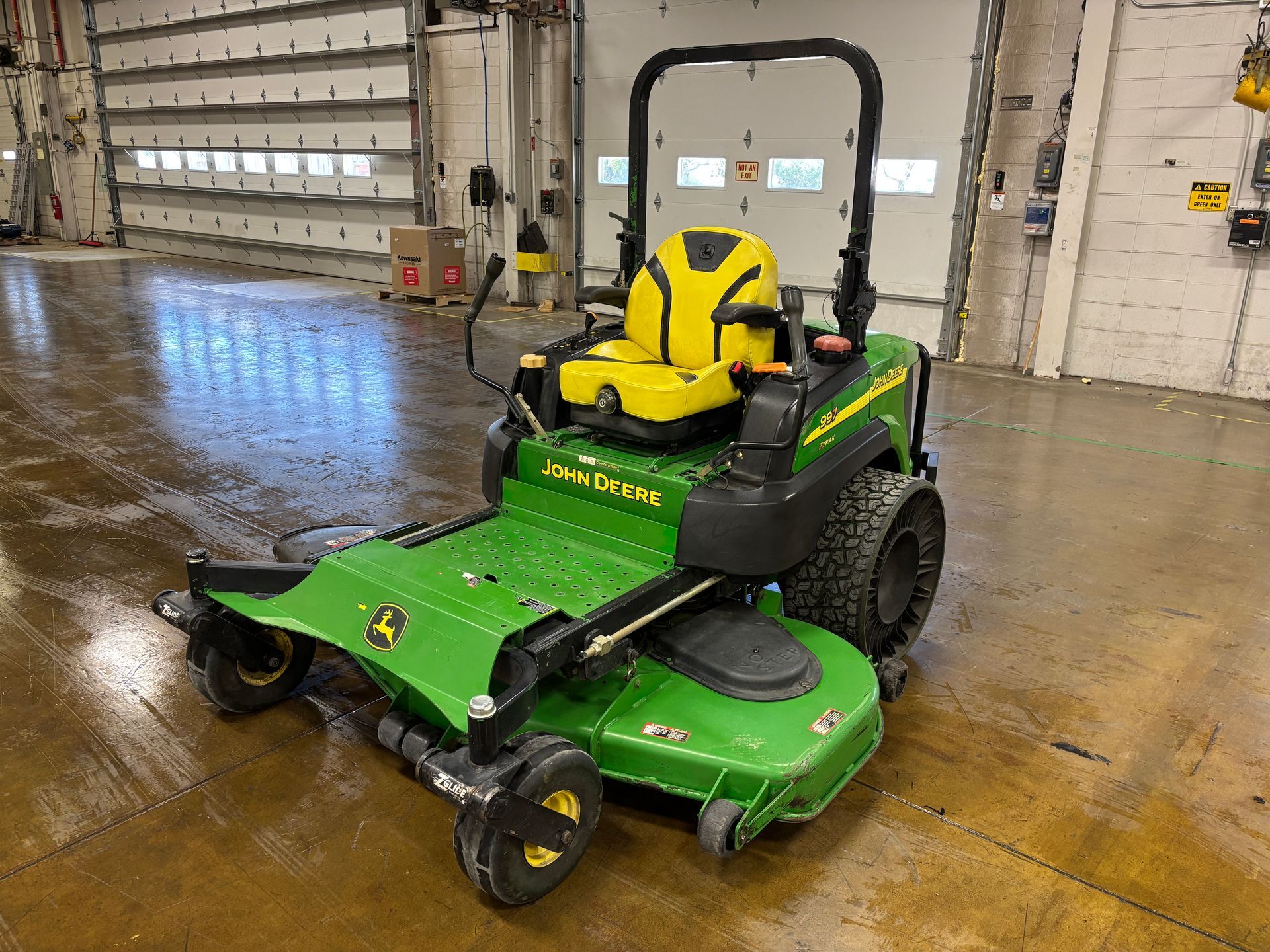 Green and yellow John Deere zero-turn lawn mower in a garage setting.