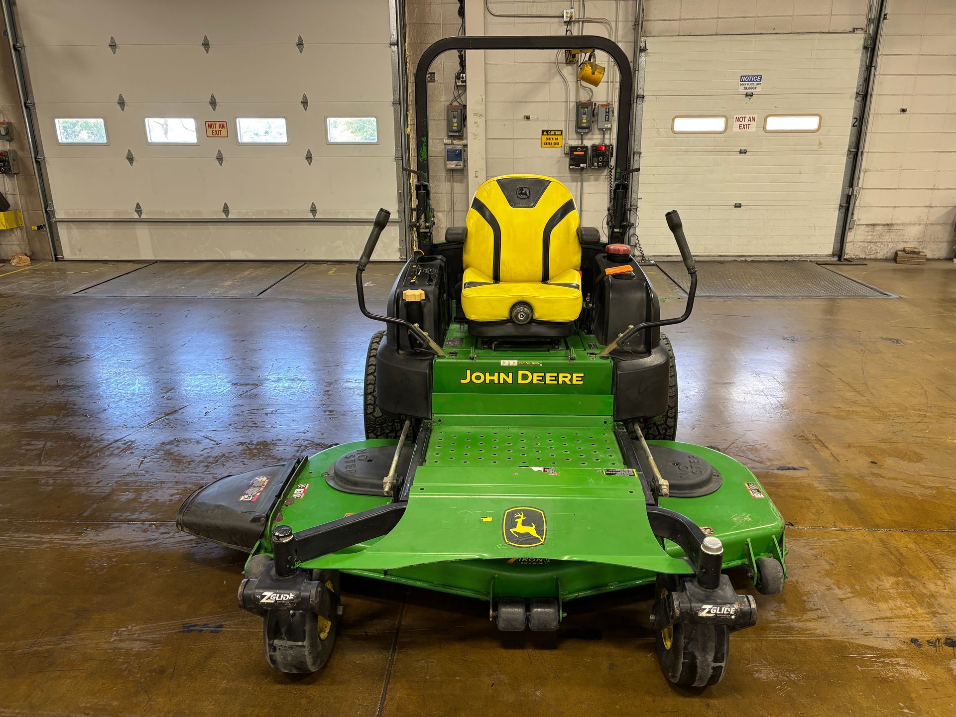Green and yellow John Deere zero-turn lawnmower in a garage.