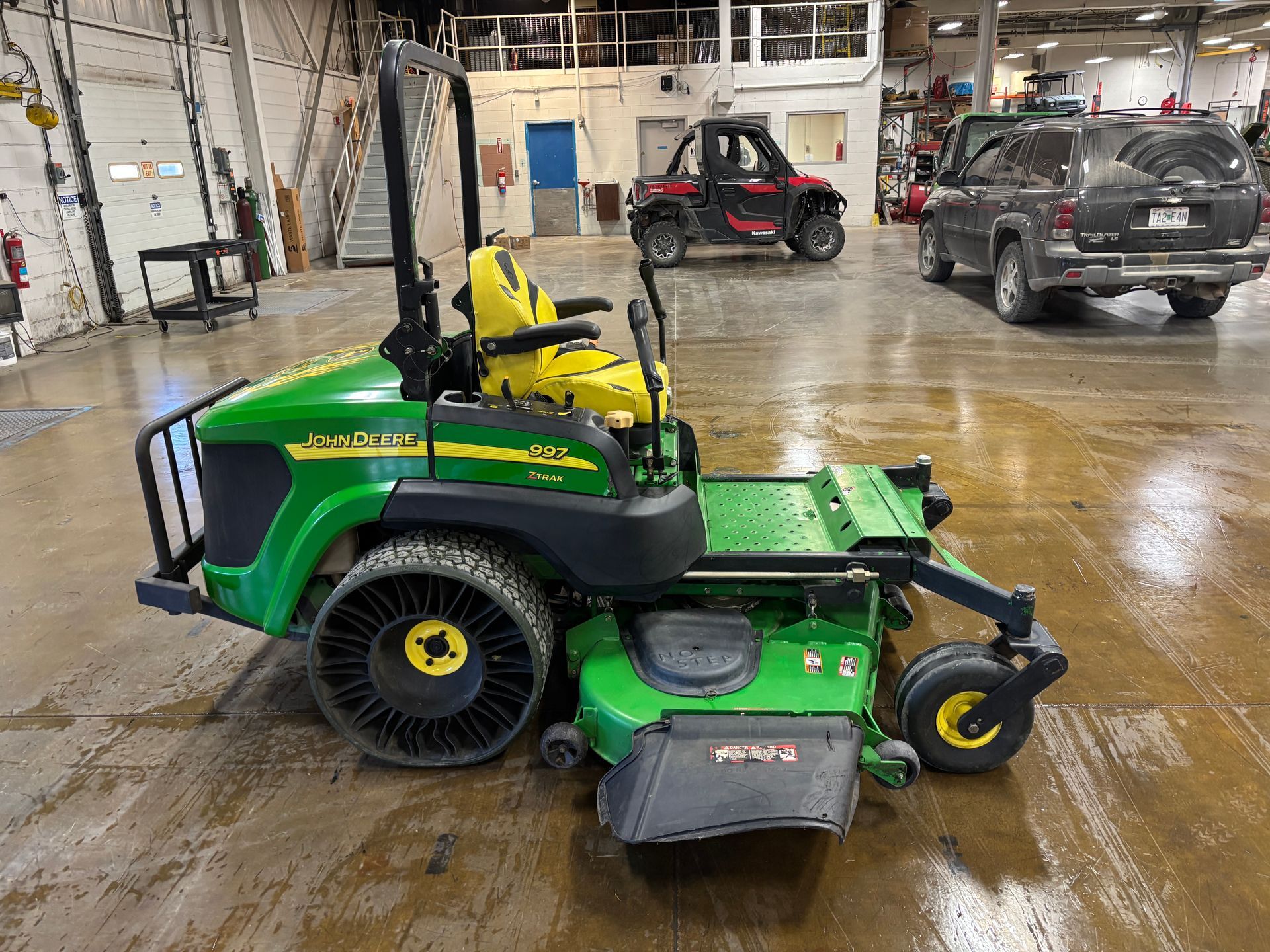 Green John Deere riding lawnmower in a garage with a yellow seat and black protective cage.