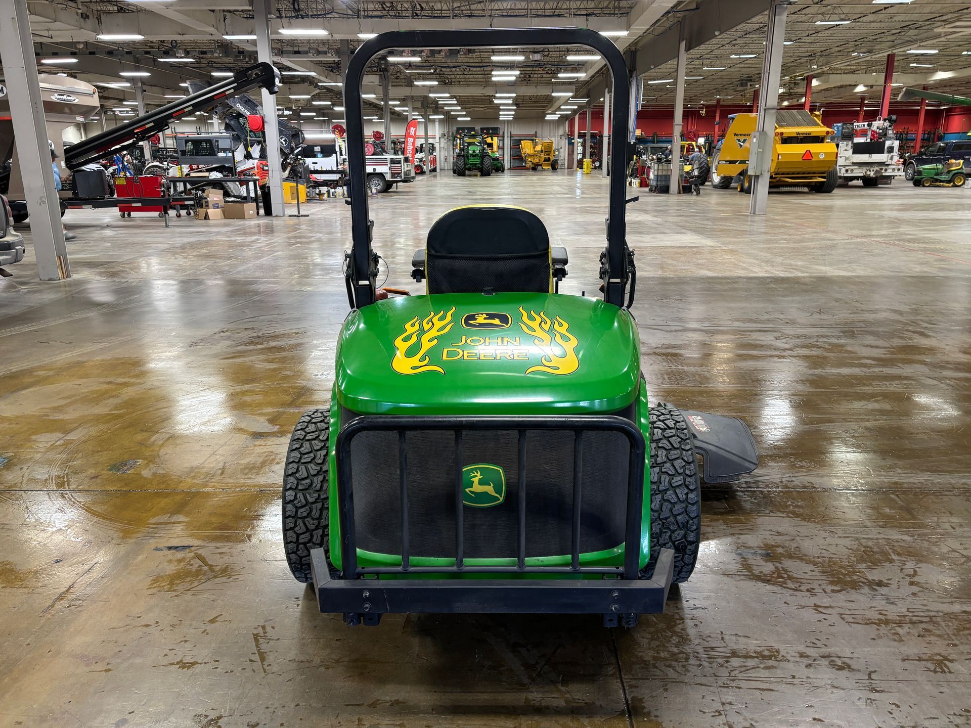 Green John Deere tractor, front view, inside a large building with other equipment.