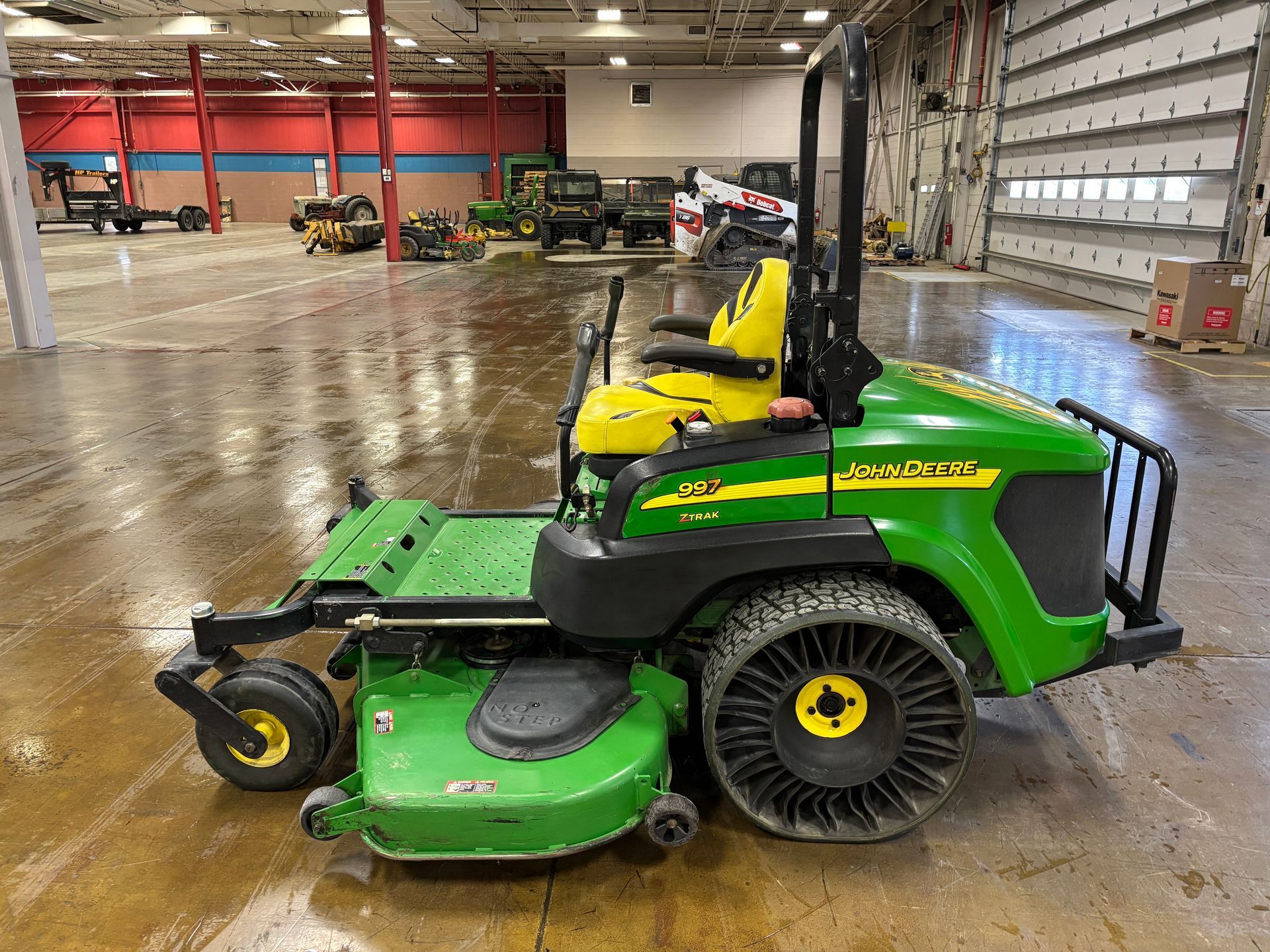 John Deere commercial zero-turn mower on a concrete floor. Green and yellow, with safety features.