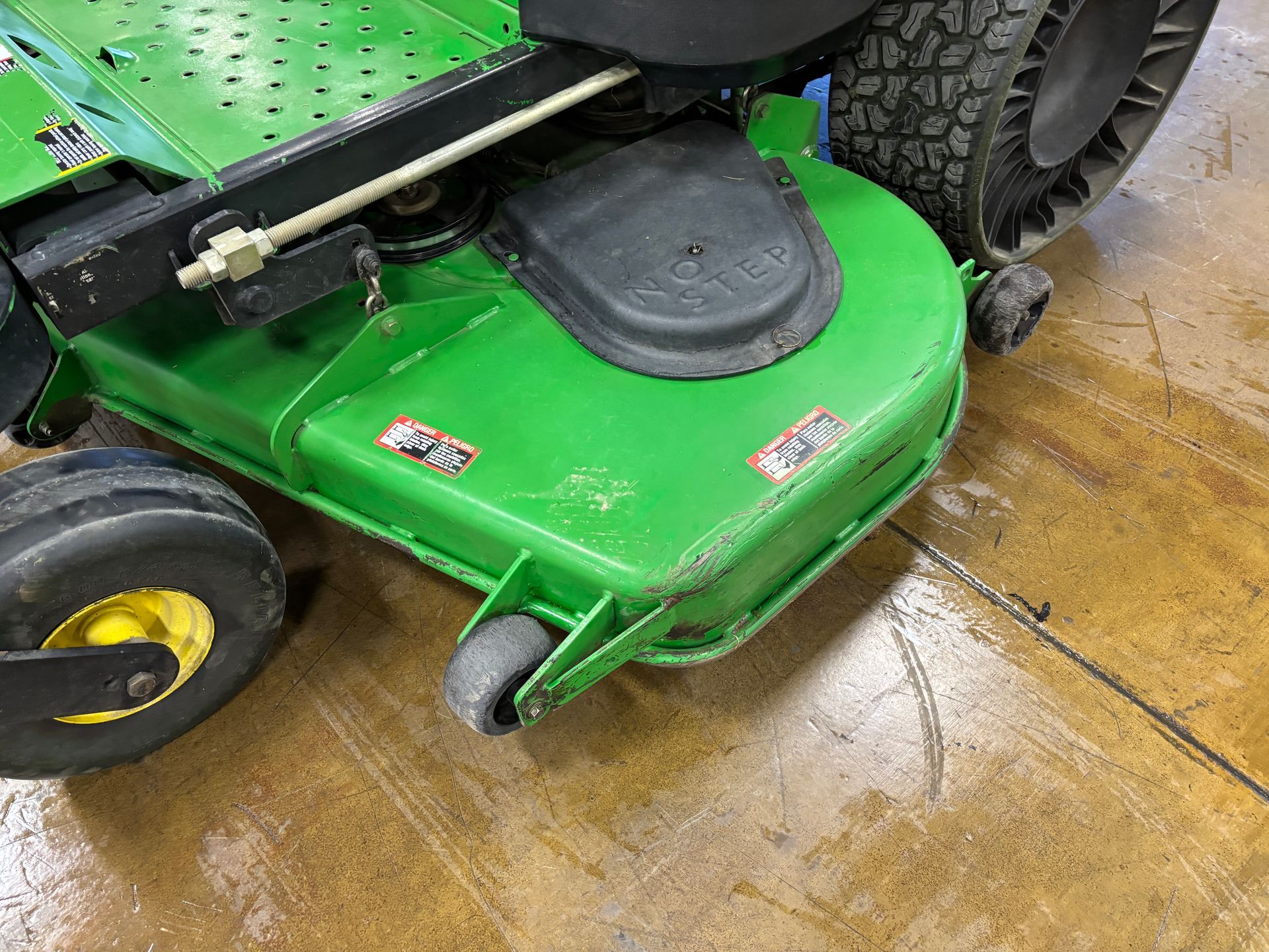 Green John Deere lawn mower deck with wheels on a concrete floor.