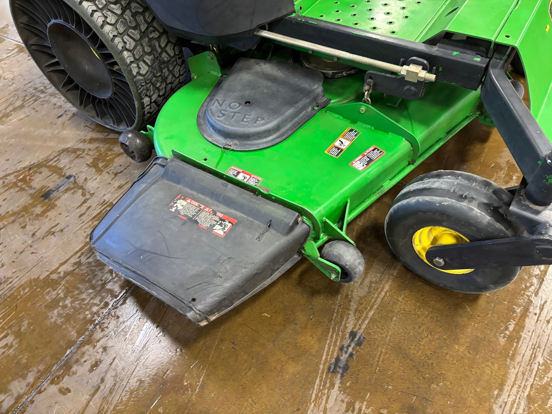 Green John Deere lawnmower deck and tire on a wood surface. Black deflector, yellow wheel.