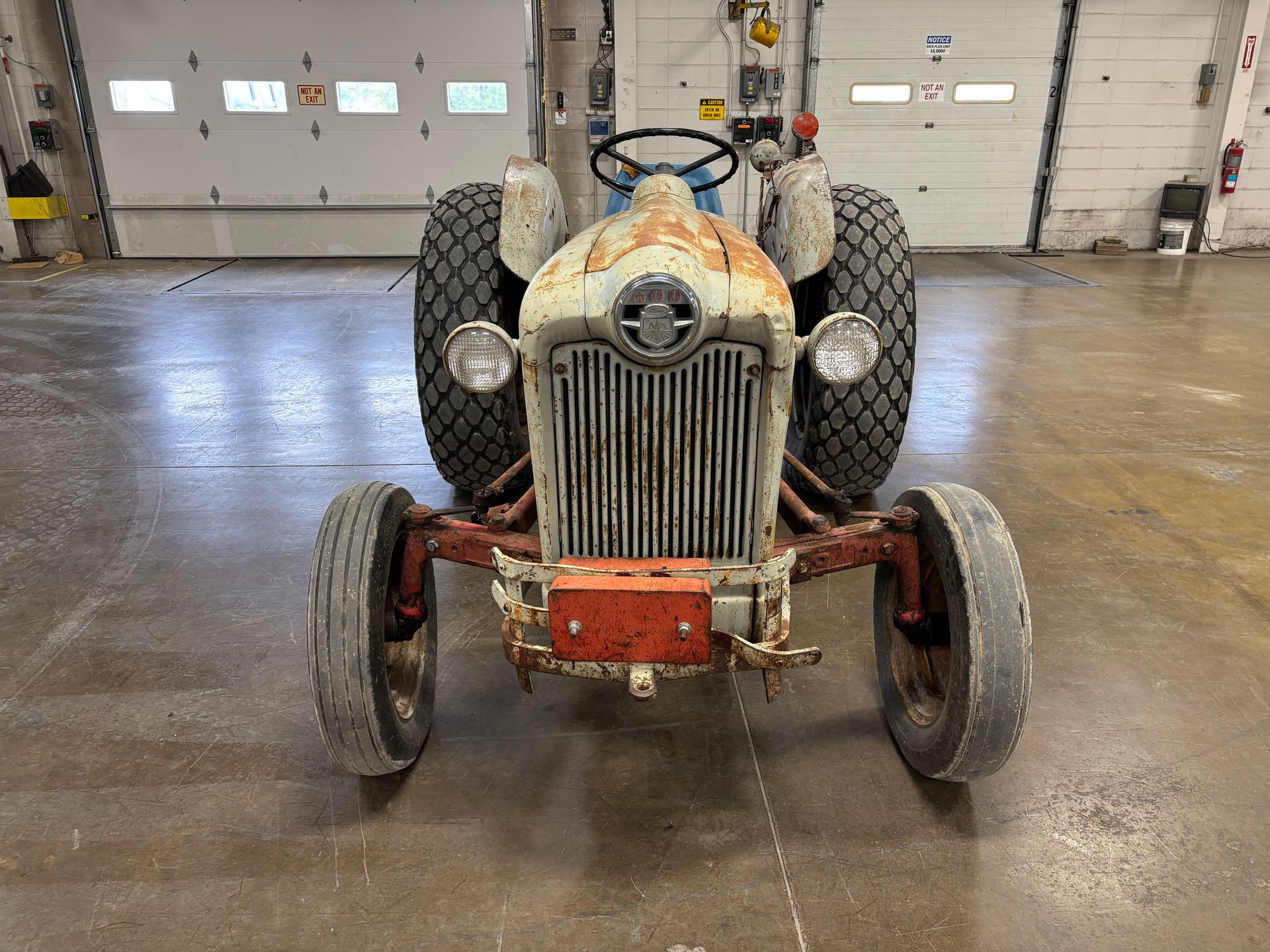 Front view of a weathered Ford tractor with a rusty red frame and large tires, parked in a garage.