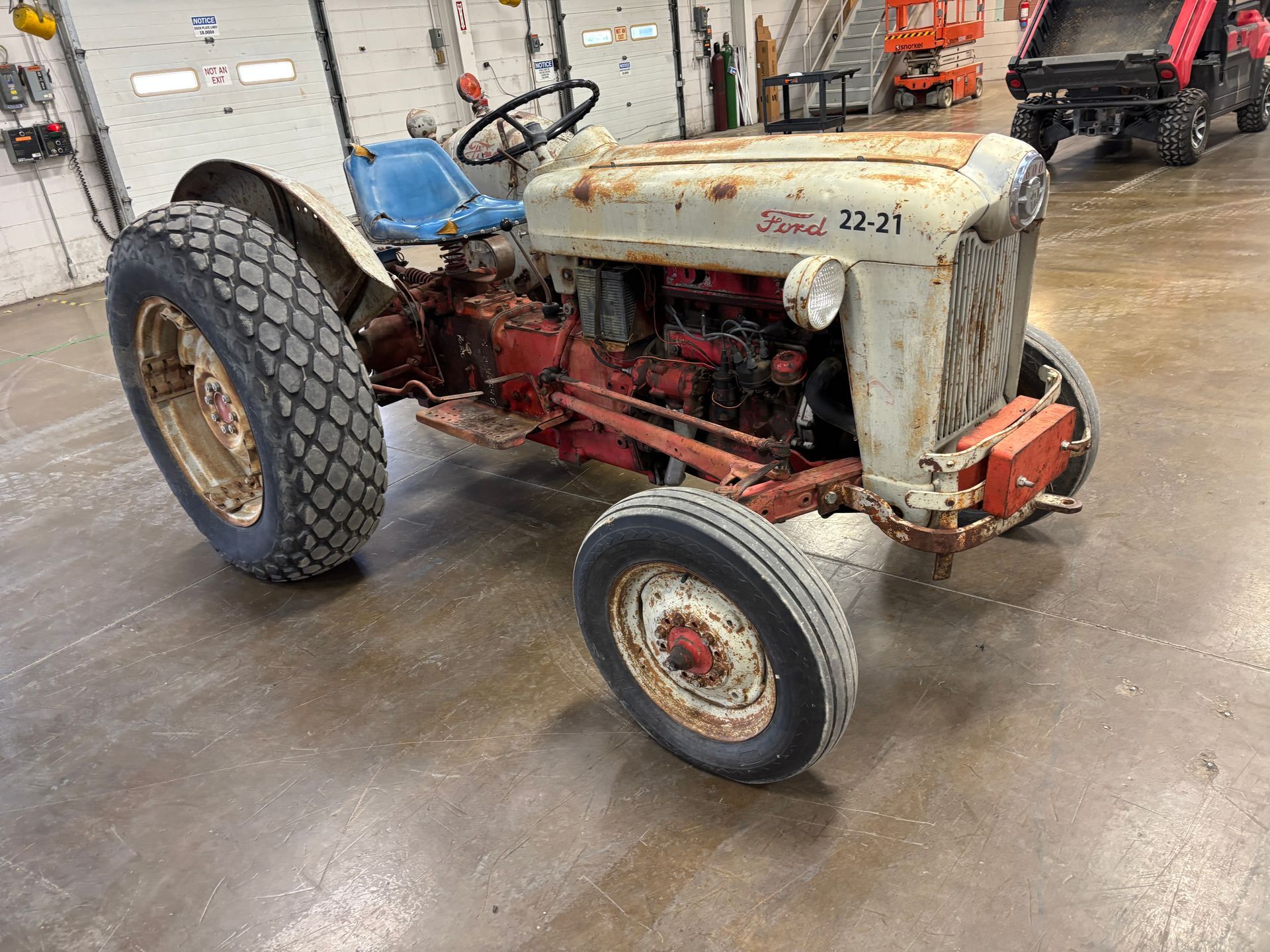 A vintage Ford tractor, faded white and red, parked on a concrete floor.
